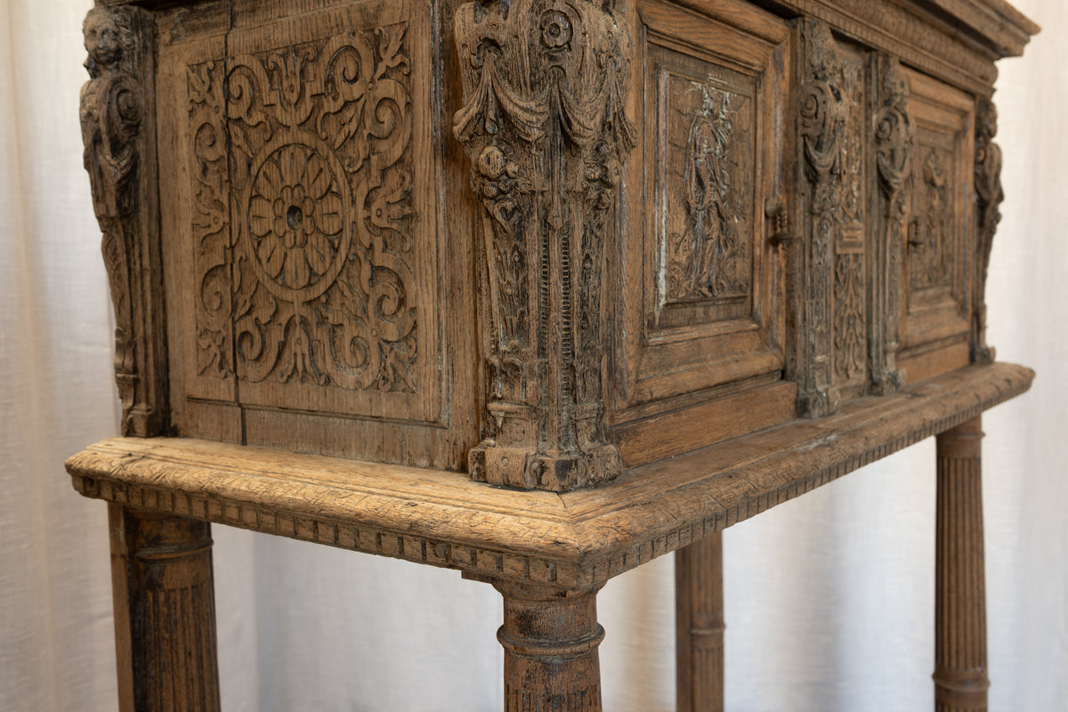 An ornate antique carved wooden chest or cabinet with detailed relief carvings, shown against a white draped backdrop.