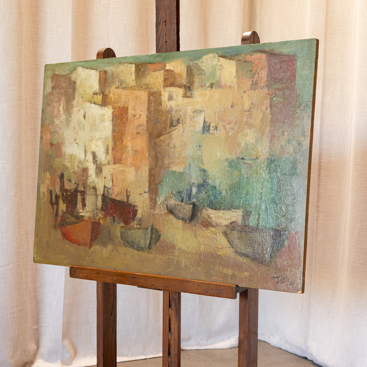 An abstract painting of boats and buildings in muted earthy tones, displayed on a wooden easel against a draped beige fabric backdrop.