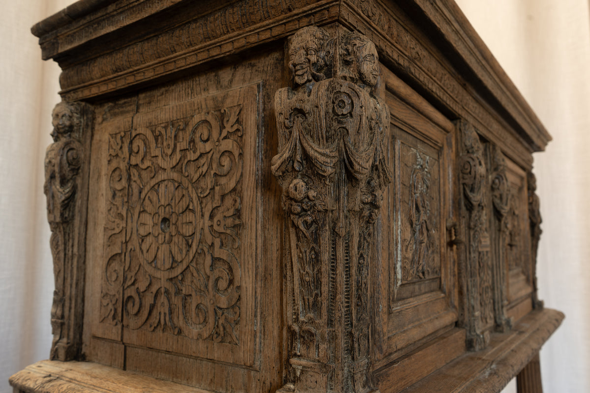 Close-up of an ornate carved wooden casket or cabinet with detailed relief carvings and decorative figures on a light neutral background.