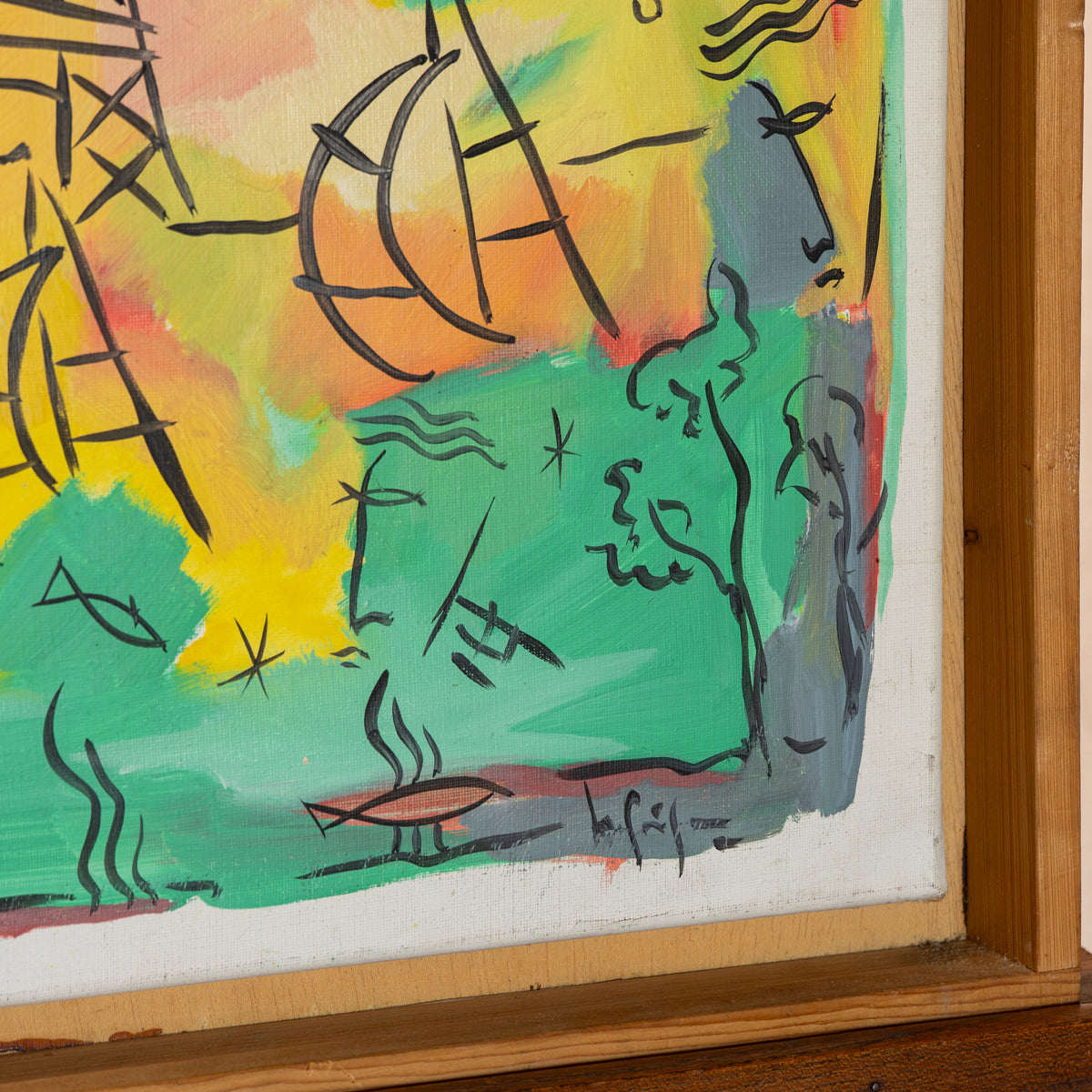 A close-up of a framed abstract painting featuring expressive black line drawings on a white ground, with a bright yellow and orange sky and green landscape elements. The wooden frame is visible around the artwork.