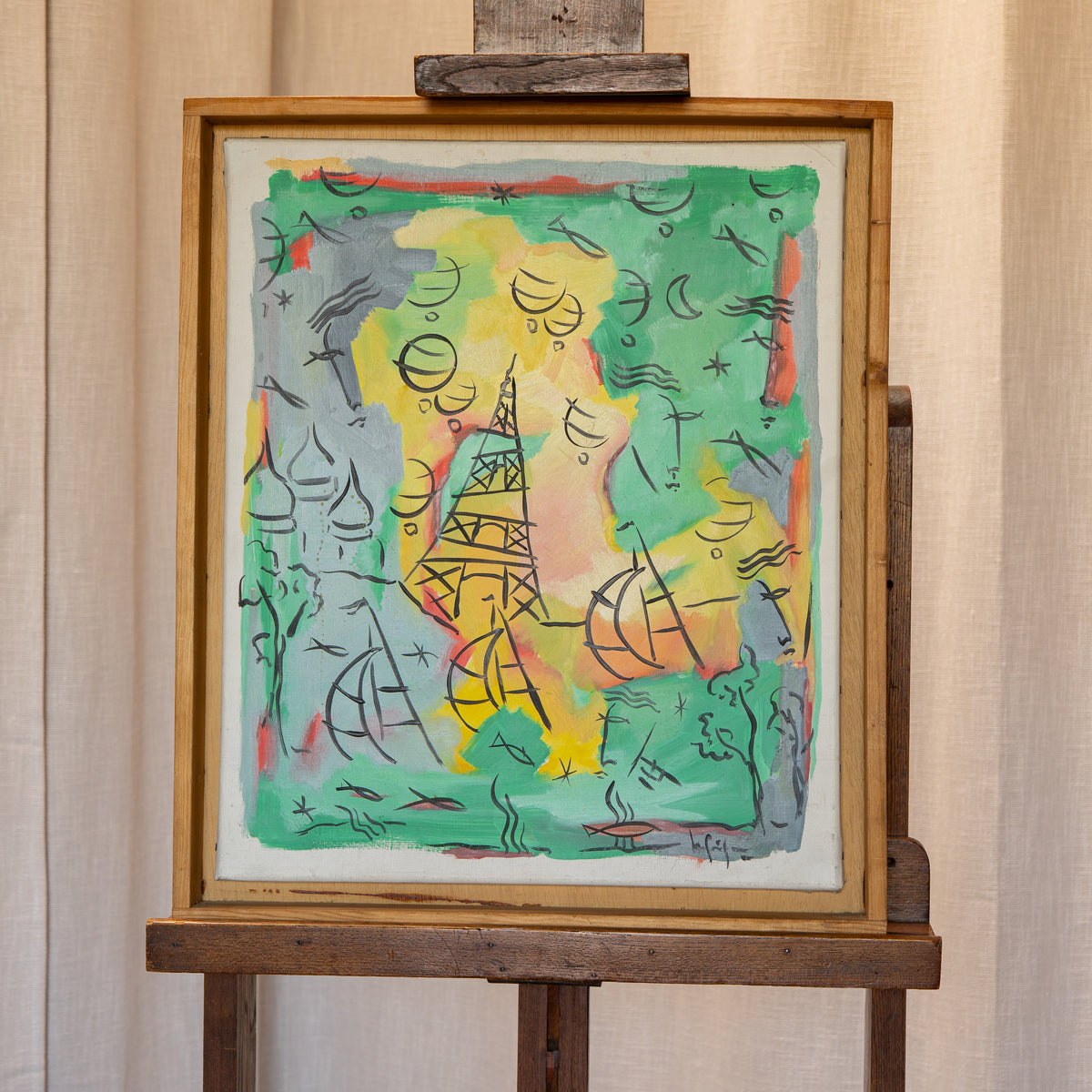 A framed abstract artwork displayed on a wooden easel against a beige curtain background. The painting features a colorful composition with green, yellow, pink, gray, and orange tones, black line details, and a white mat border.