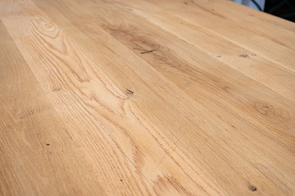 Close-up of a light natural wood tabletop with visible grain, knots, and a smooth finish.