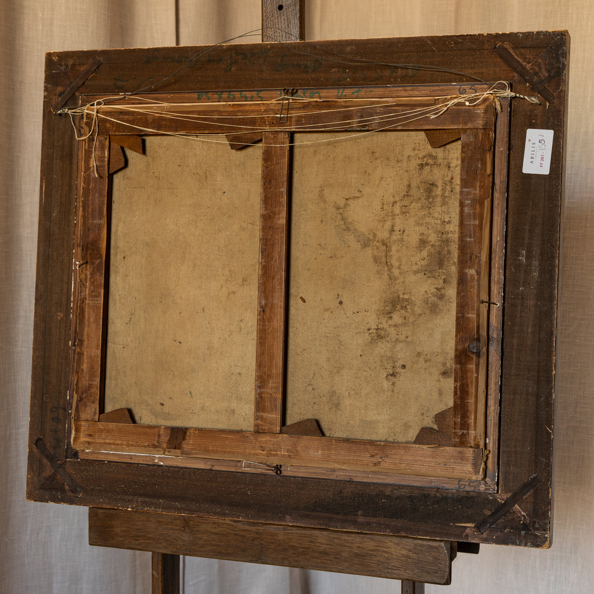 The back view of a vintage wooden picture frame mounted on an easel, showing the canvas backing and hanging string.