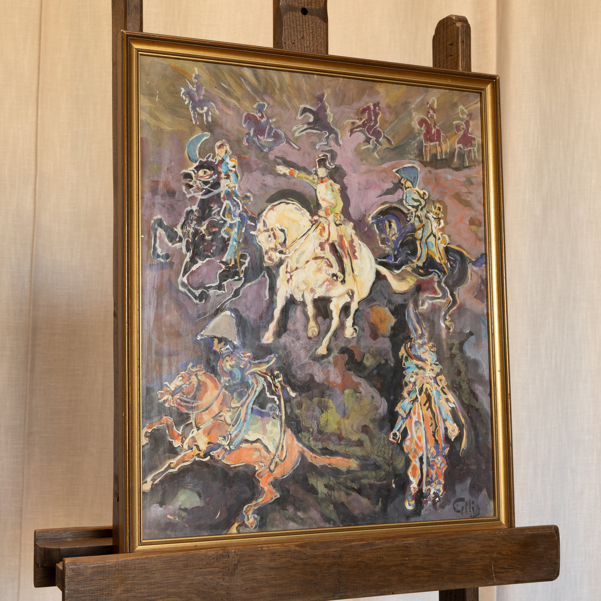 A framed painting on an easel, depicting stylized riders on horseback in expressive brushstrokes with a gold-toned frame against a light wood-paneled wall.