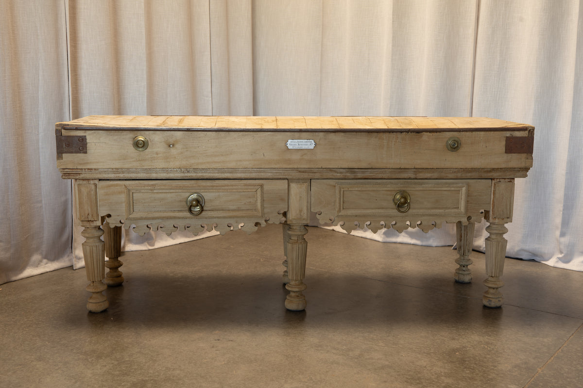 A rustic, distressed wooden chest or bench with two drawers, turned legs, and brass hardware, set against a neutral draped curtain backdrop.