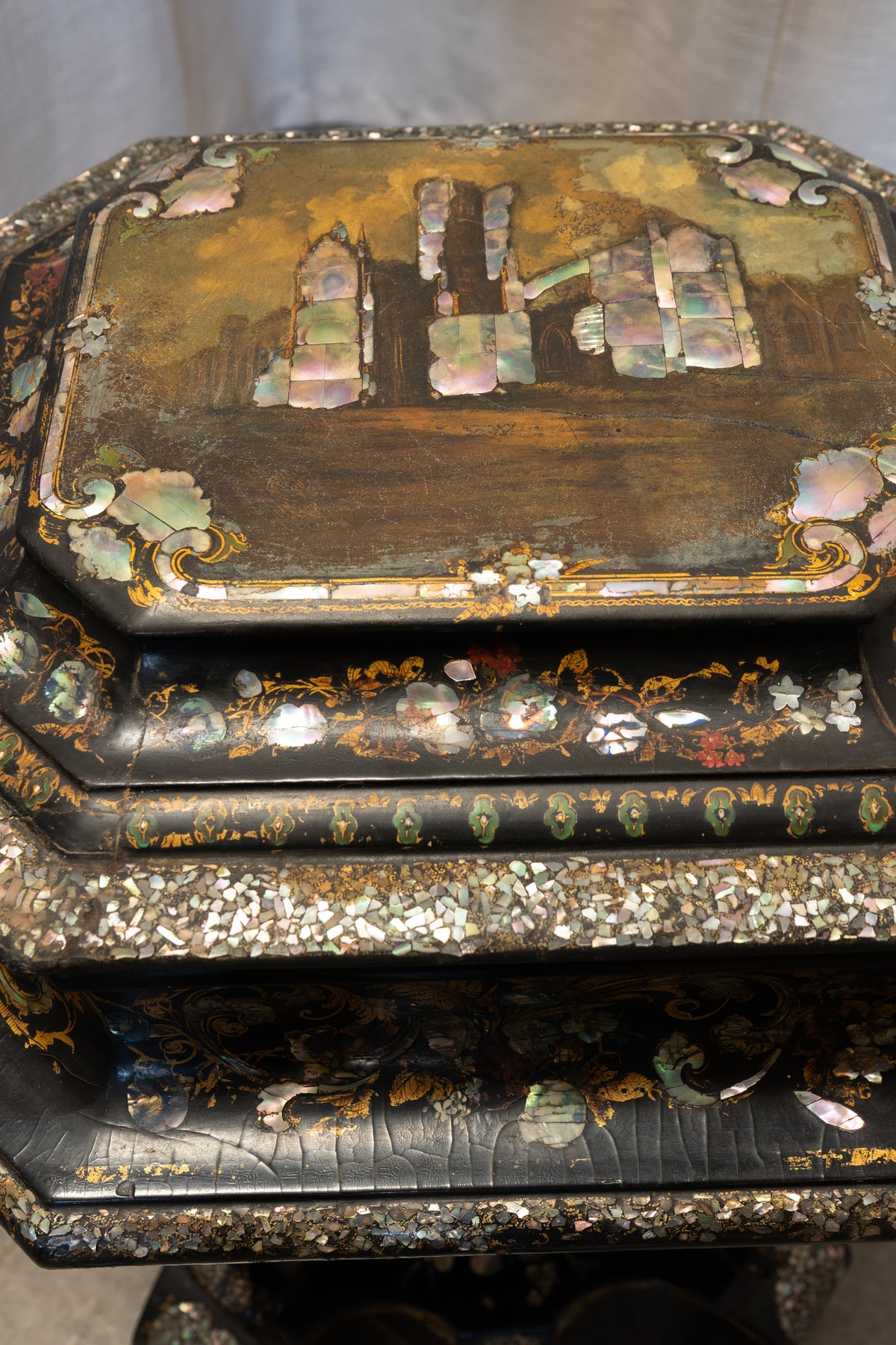 An ornate vintage black lacquer box decorated with iridescent mother-of-pearl inlay, featuring a detailed architectural scene on the lid and floral motifs.