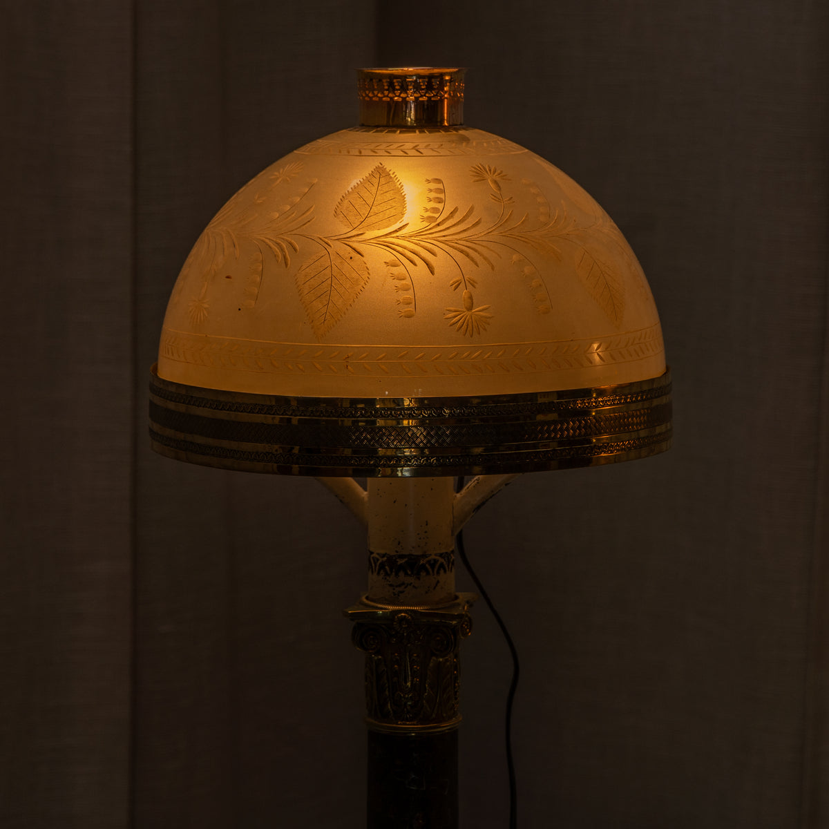 A vintage-style table lamp with a glowing warm yellow dome shade featuring embossed floral patterns, set against a dark background.