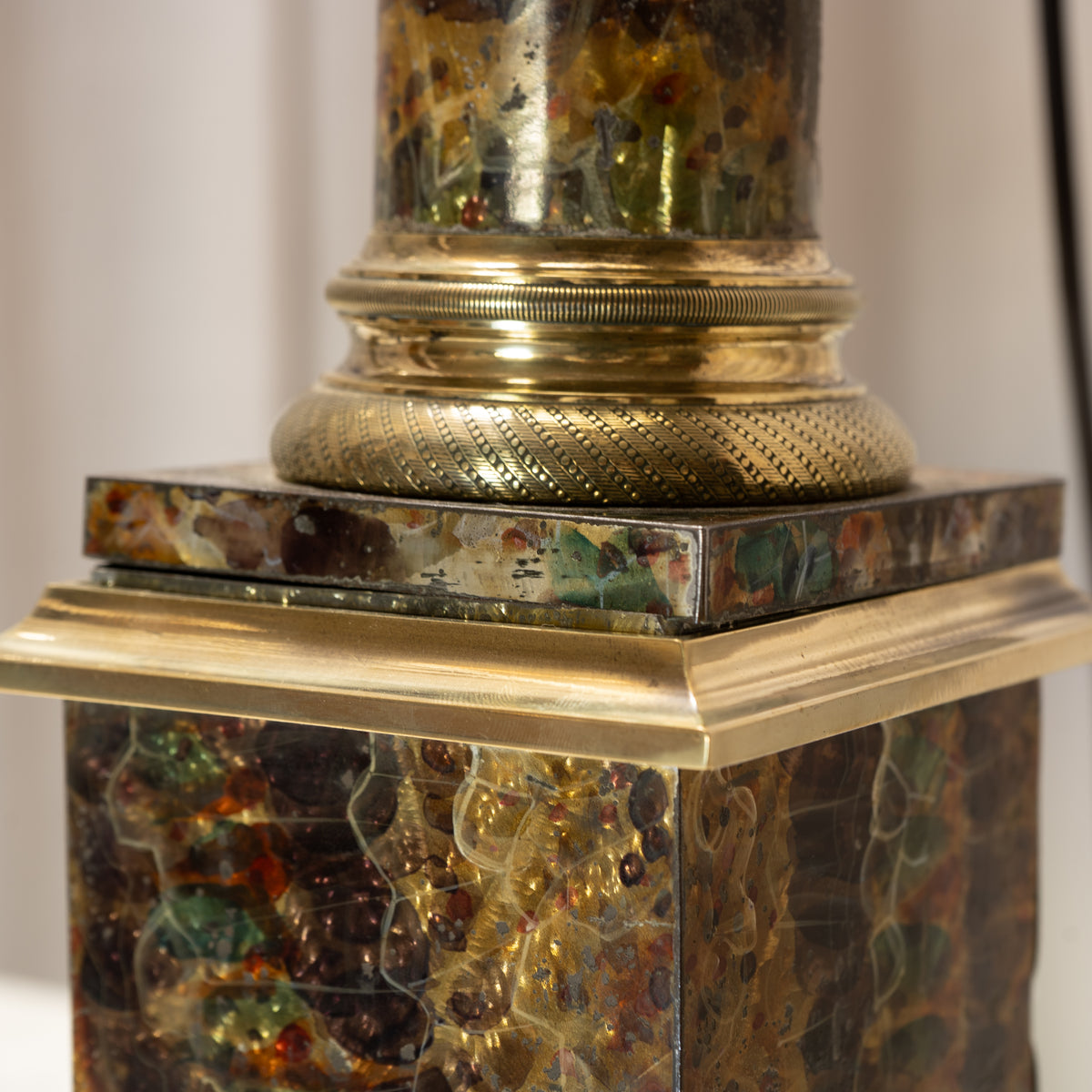 Close-up of a decorative lamp base with a gold-toned metal collar and a marbled mosaic stone or glass pedestal in amber, brown, green, and gold tones.