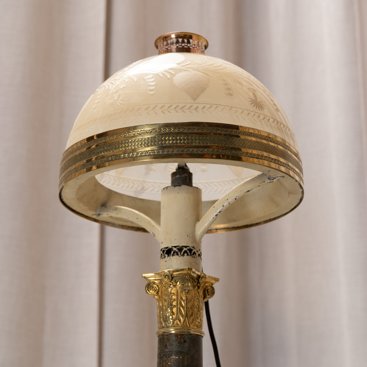 An ornate vintage-style floor lamp featuring a cream-colored glass dome shade with etched floral motifs and a decorative gold band, supported by a dark column with an ornate gold collar.