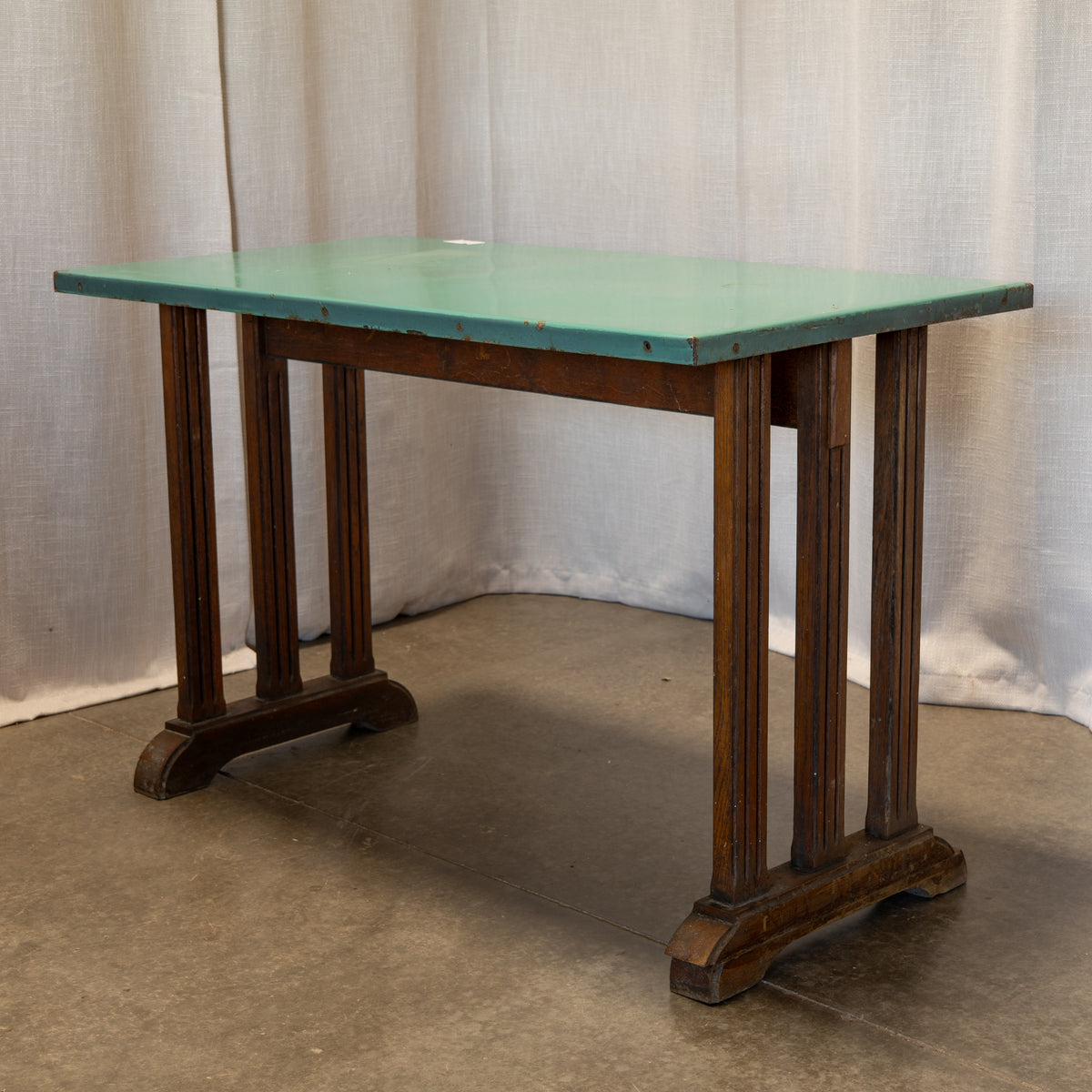 A dark brown wooden table with a distressed light green top, photographed against a draped beige fabric backdrop.