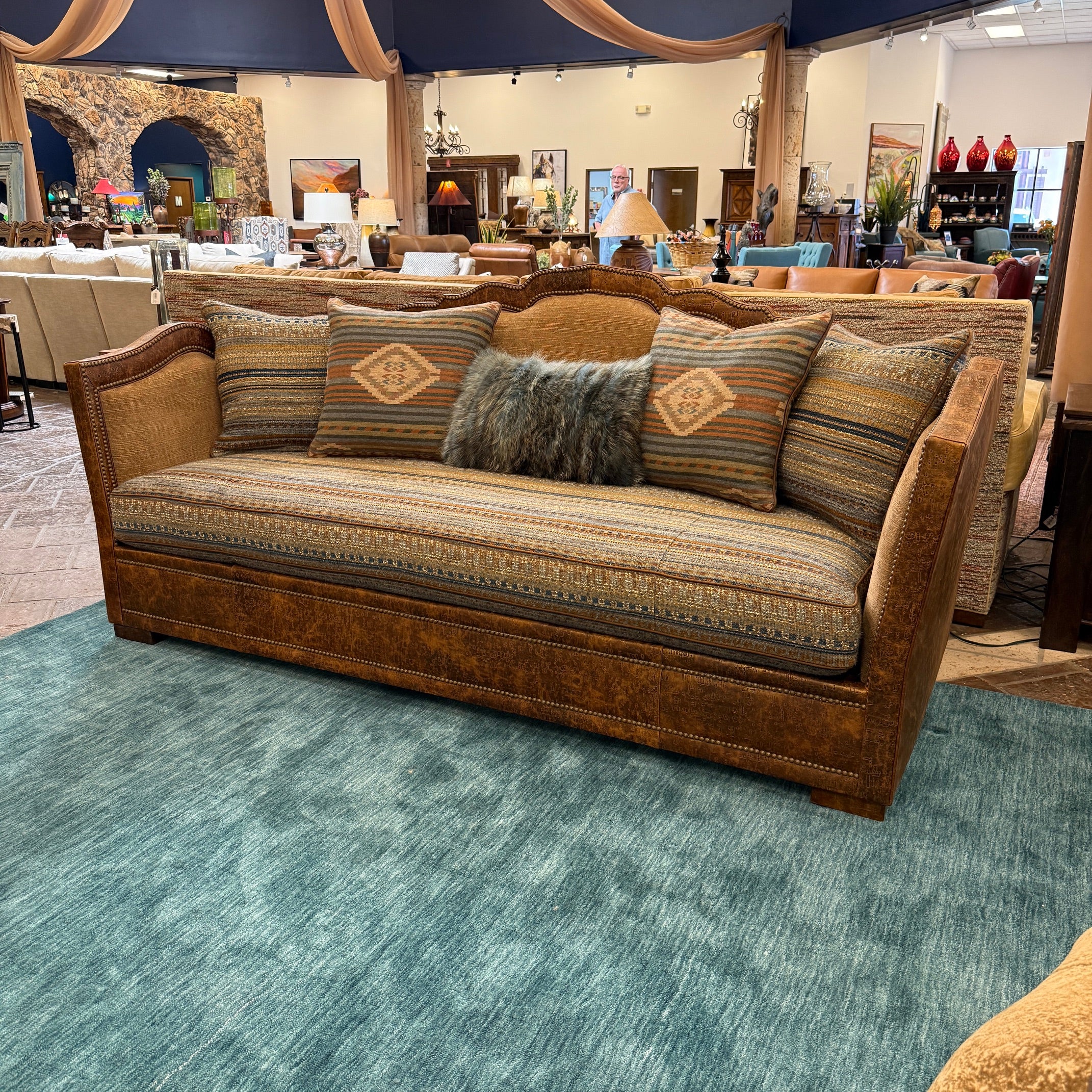 Brown sofa with patterned cushions on a blue carpet in a showroom setting.
