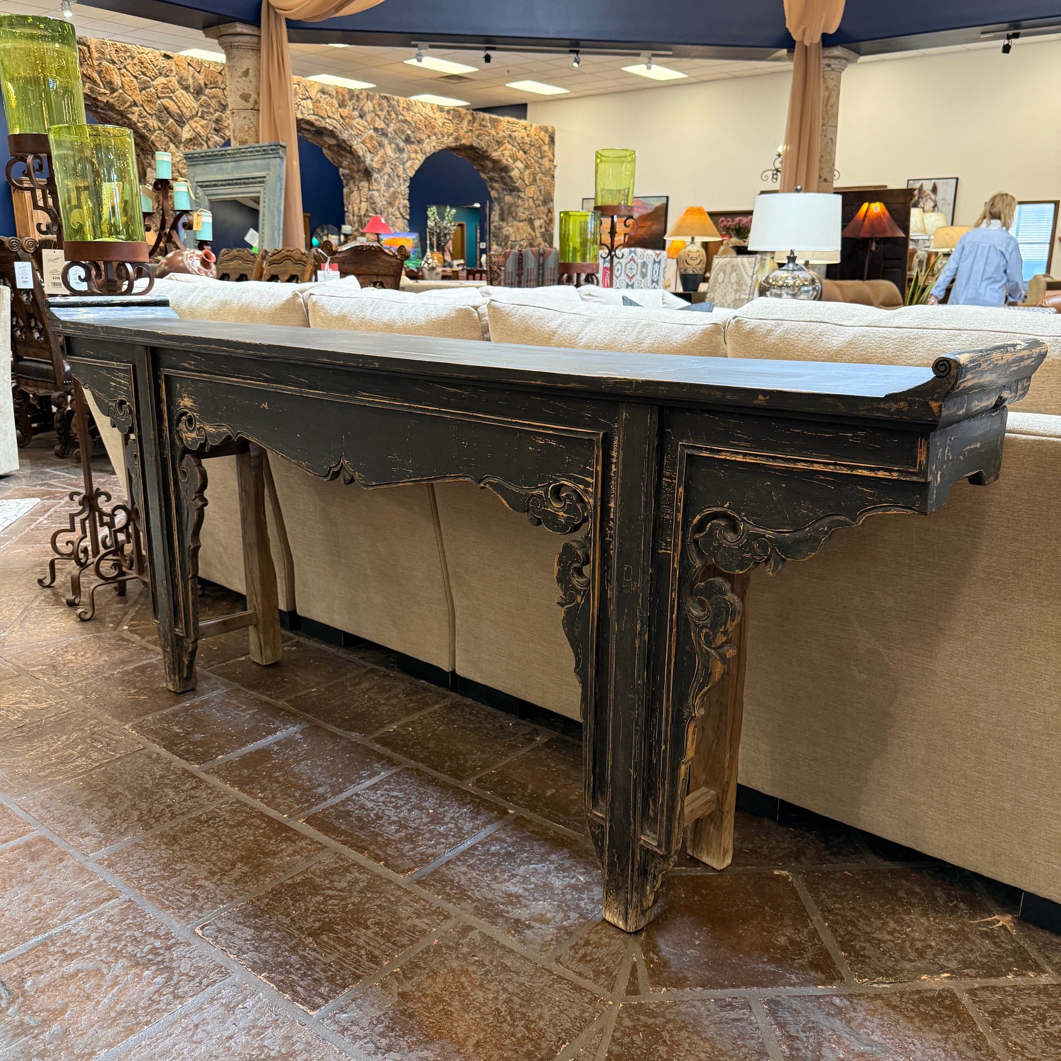 Decorative wooden table in a showroom setting with furniture and decor items in the background.