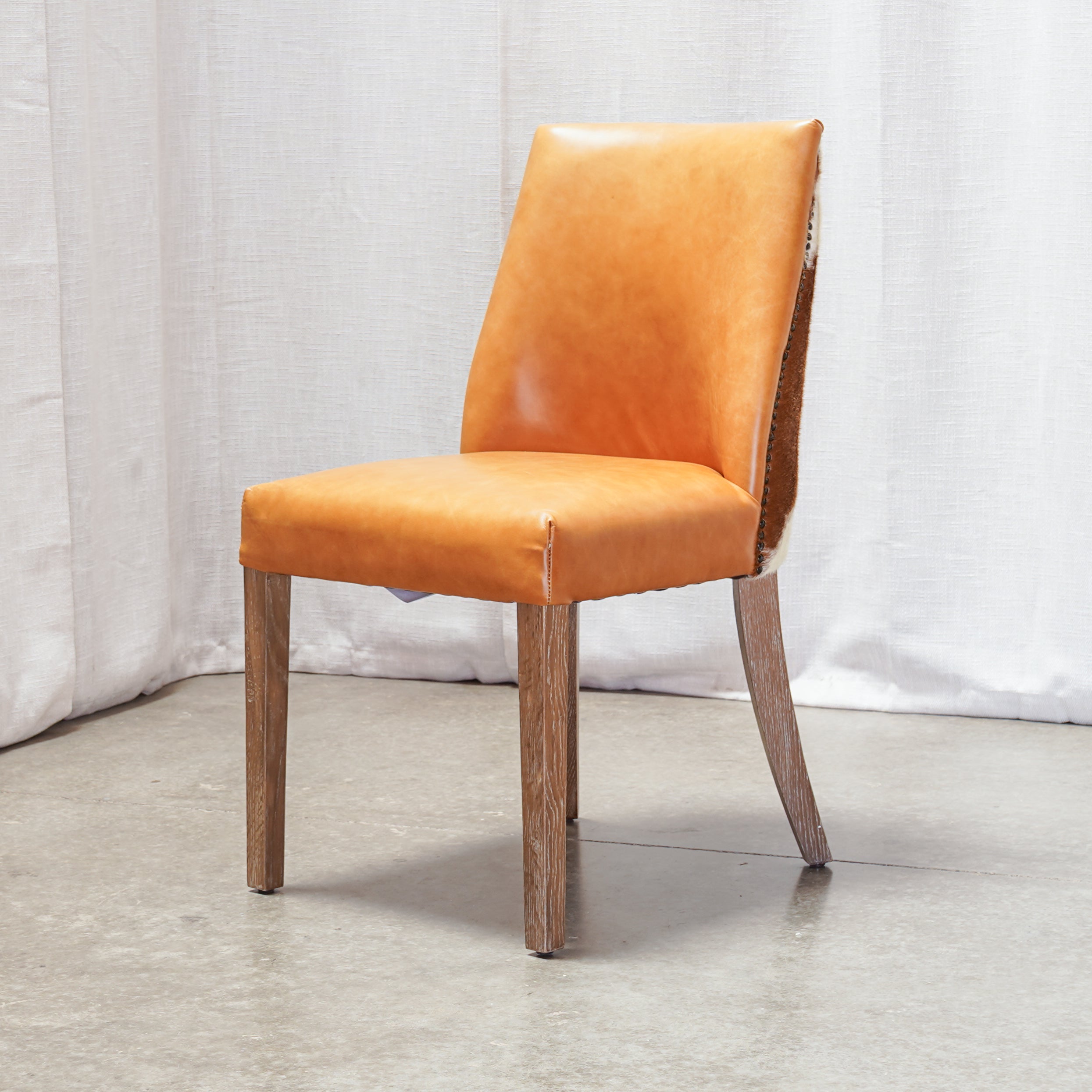 An orange upholstered dining chair with a wooden frame and tapered legs, shown against a white curtain backdrop.