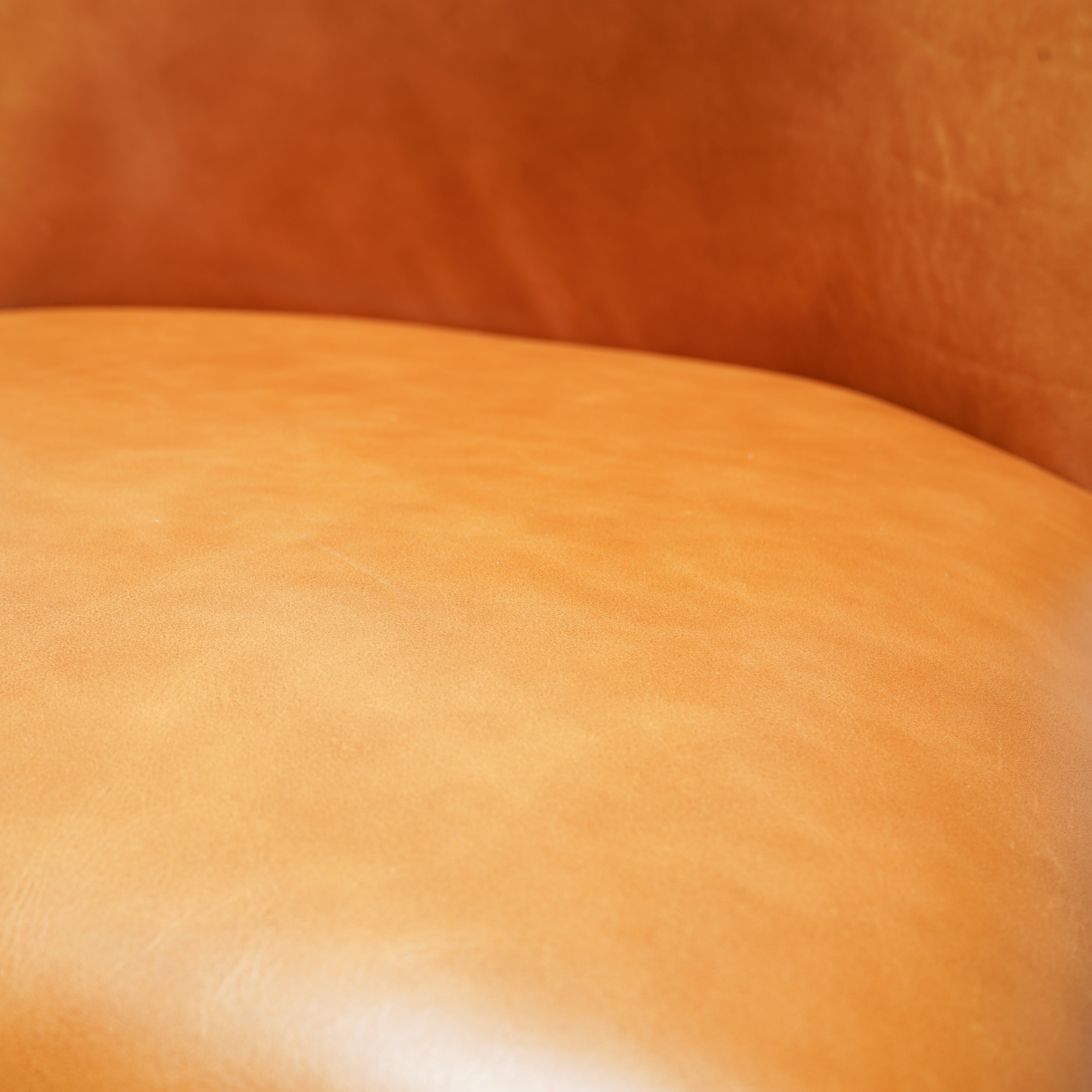 Close-up of a smooth tan leather surface with warm orange-brown shading in the background.