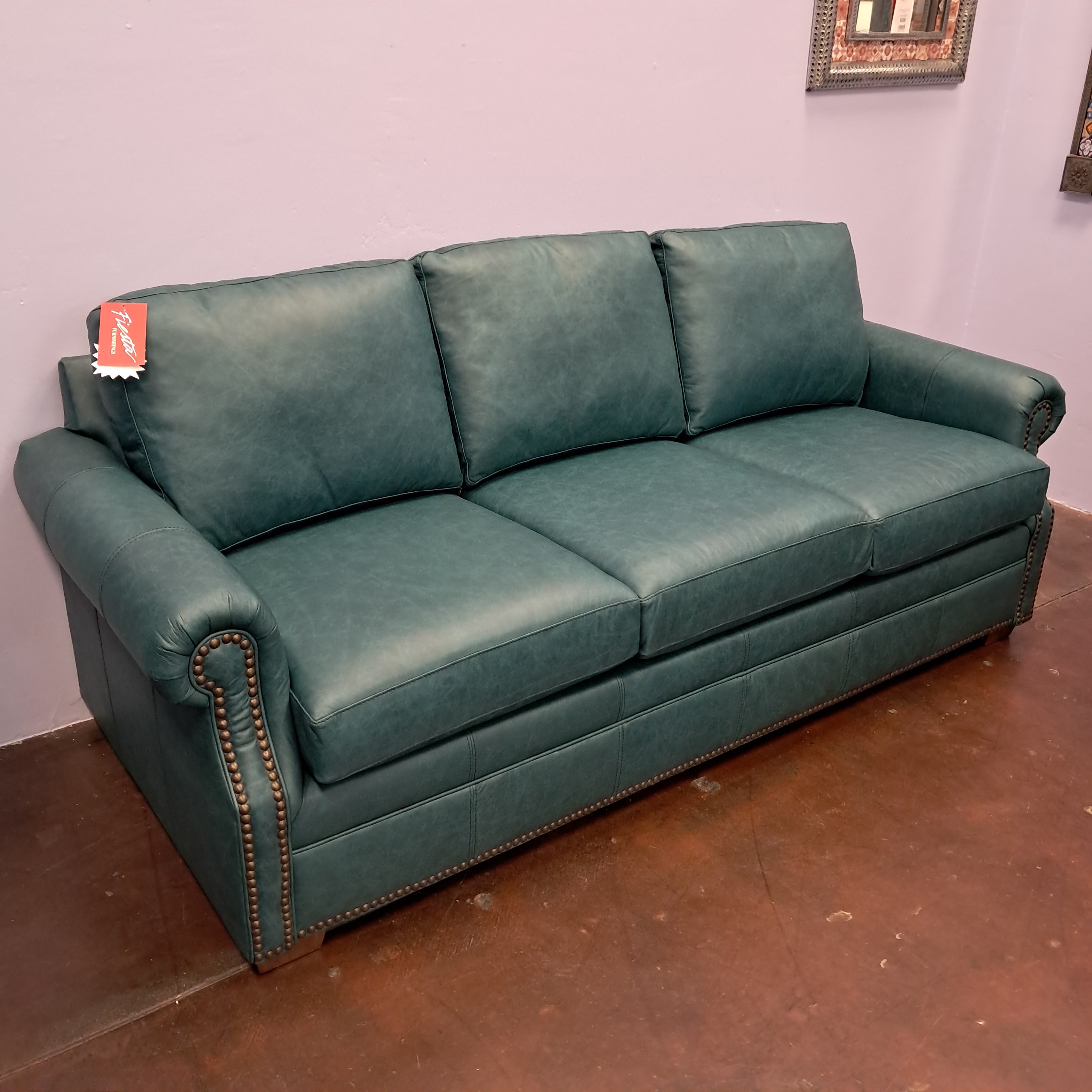 Green leather sofa in a room with a purple wall and wooden floor.