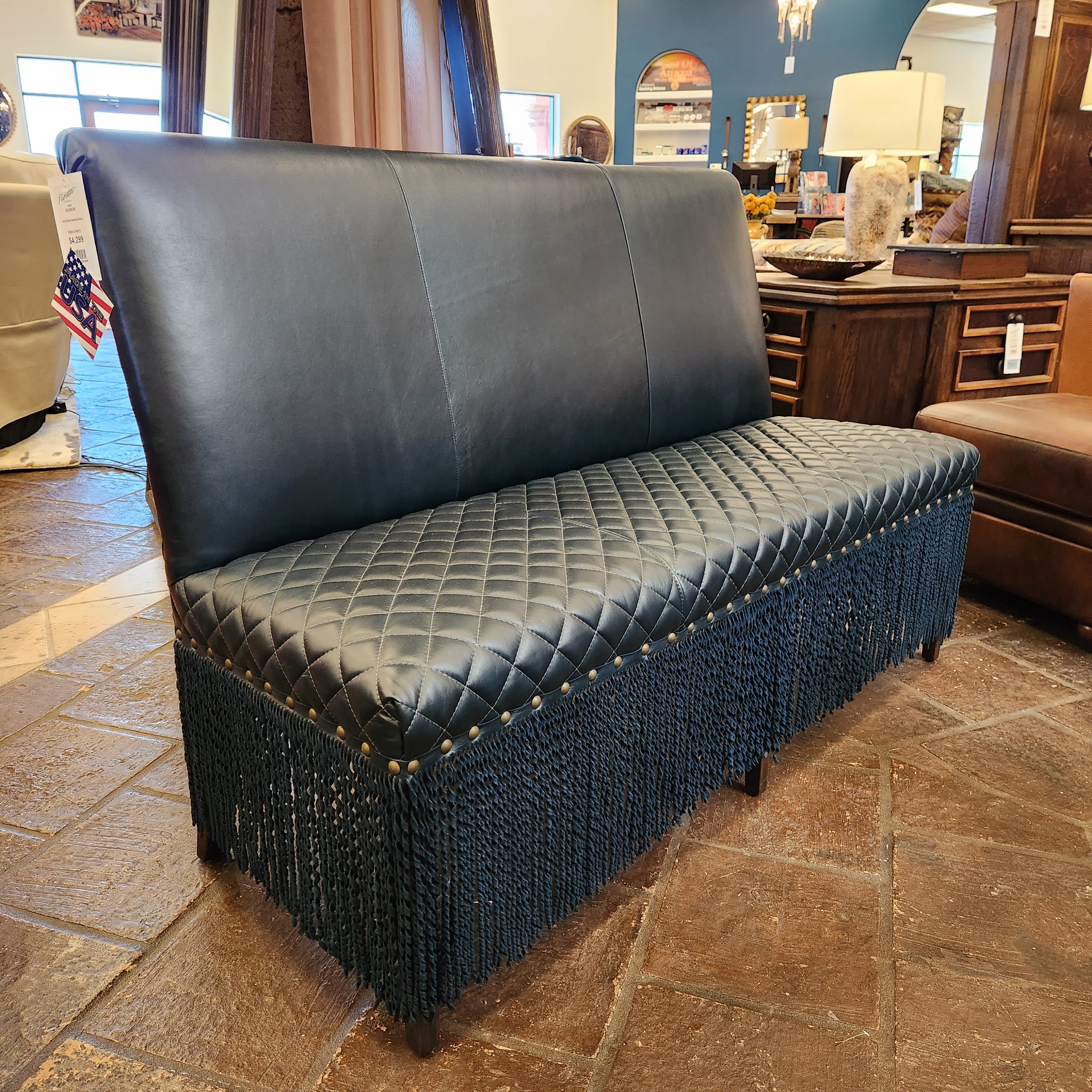 Navy leather bench with quilted design and gold studs in a room with wooden furniture and a stone wall.