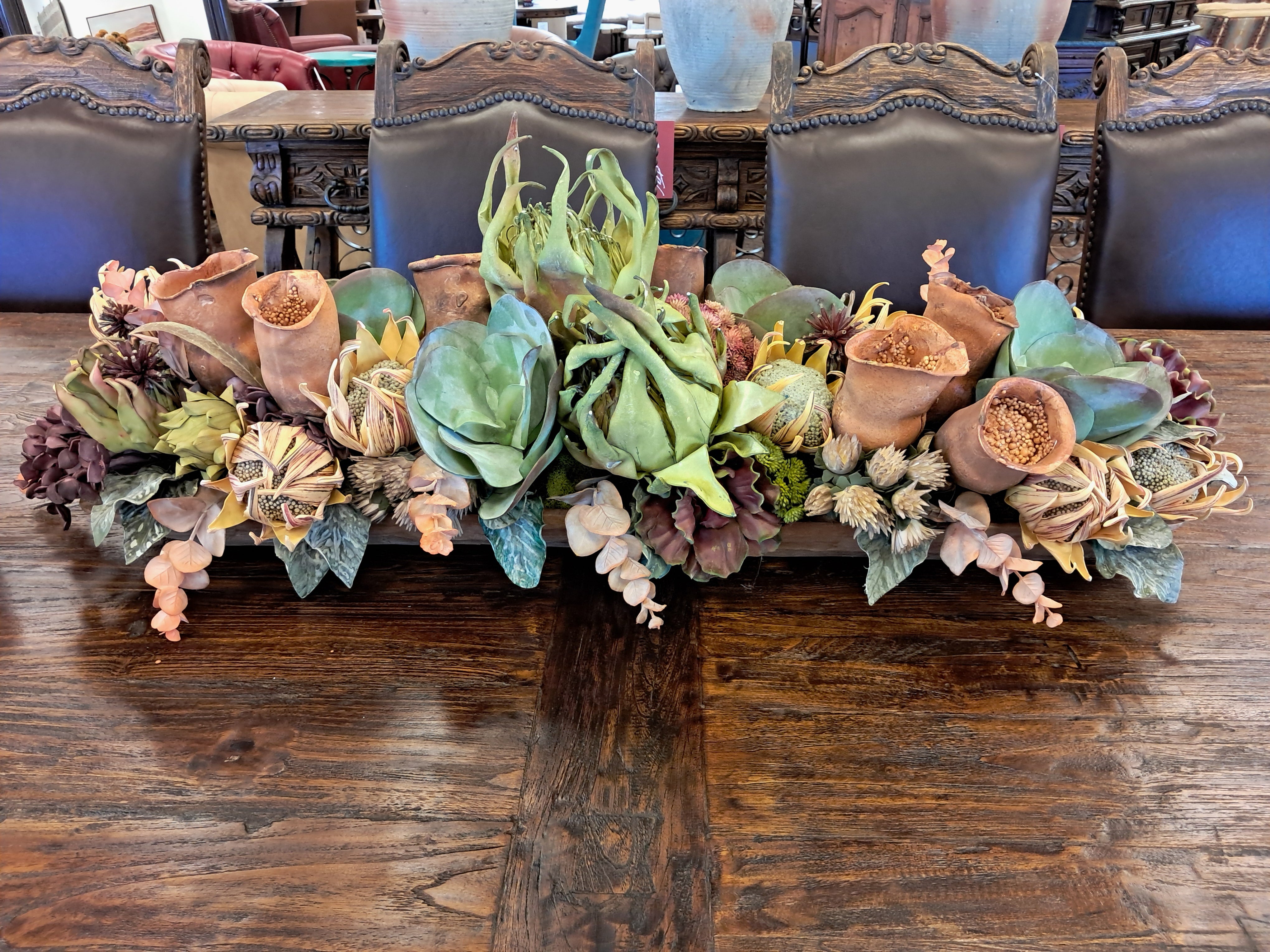 Decorative floral arrangement on a wooden table with ornate chairs in the background.