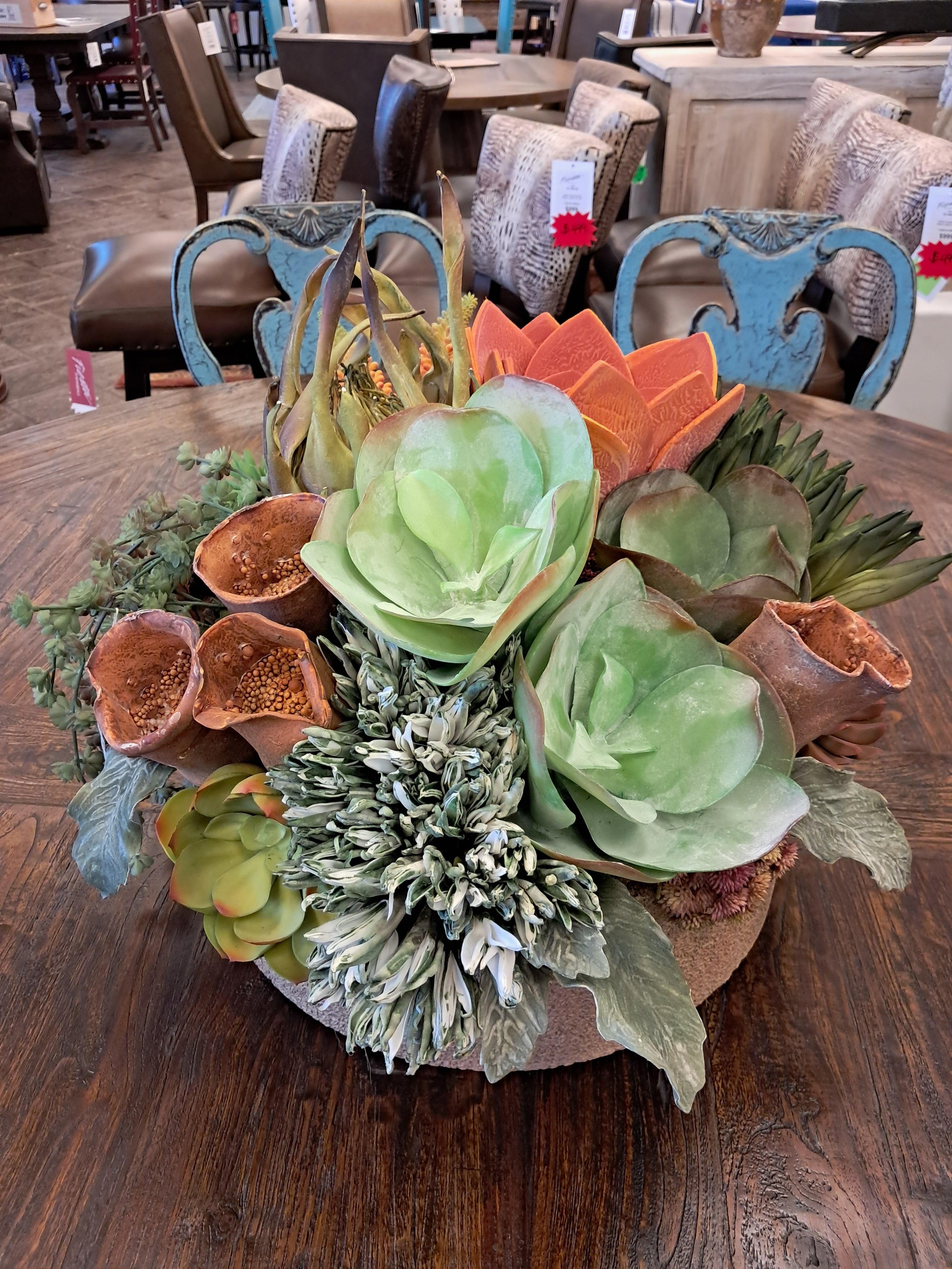 Decorative arrangement of succulents and greenery on a wooden surface with a store interior in the background.