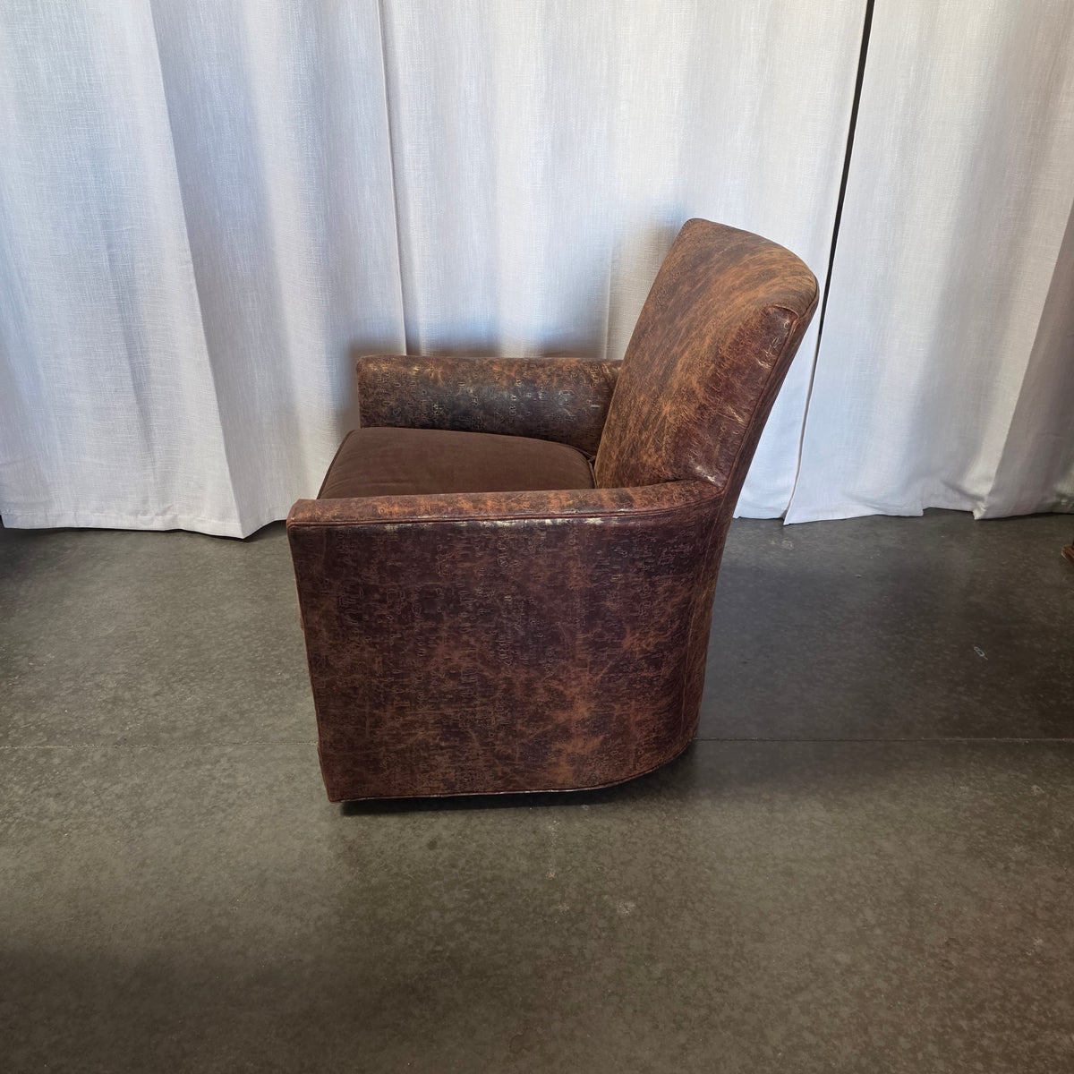 A vintage-style brown leather armchair with a distressed, heavily cracked patina, shown from a side angle against a white curtain backdrop.