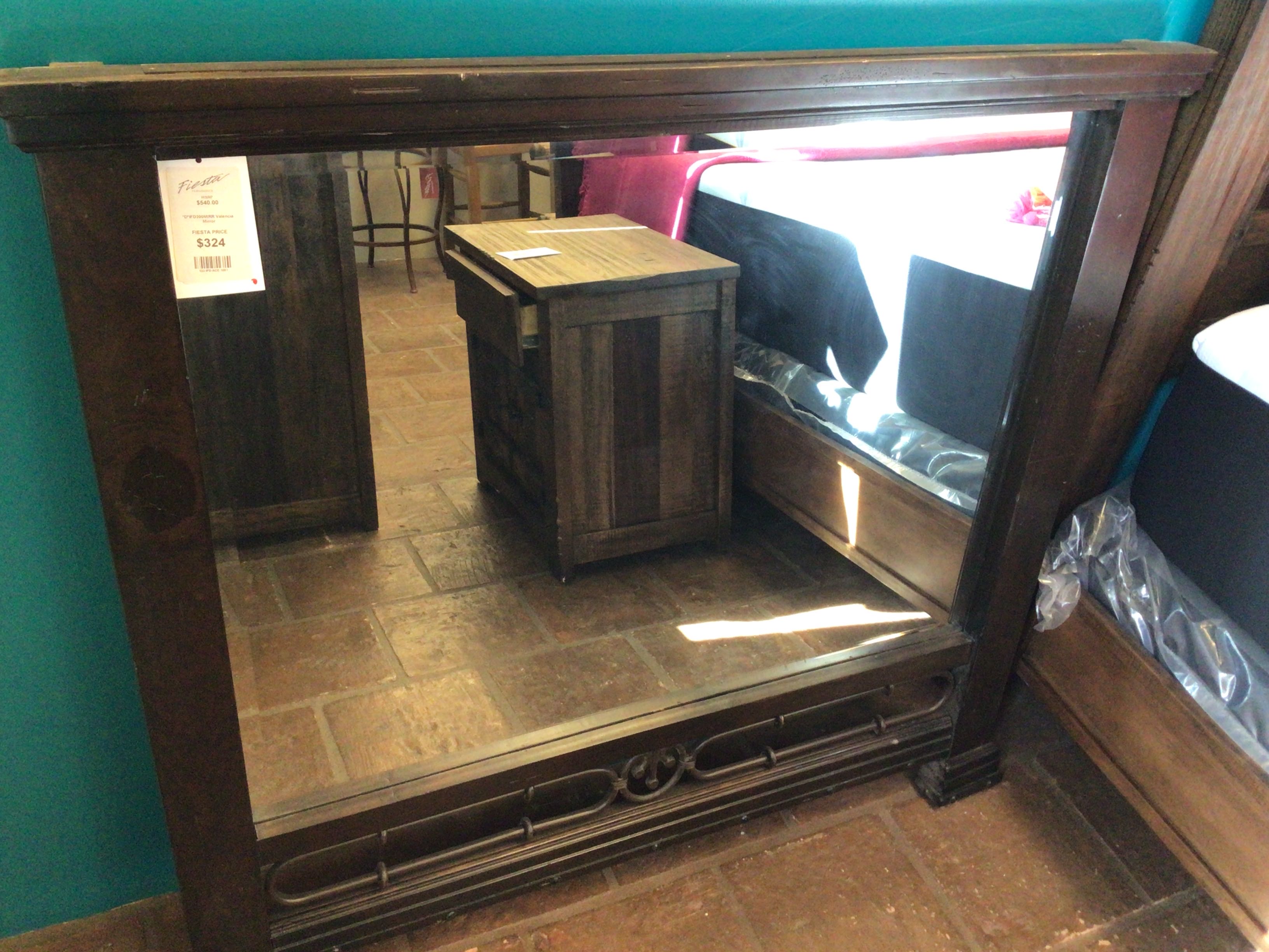 Wooden entertainment console with mirror on a tiled floor against a teal wall.
