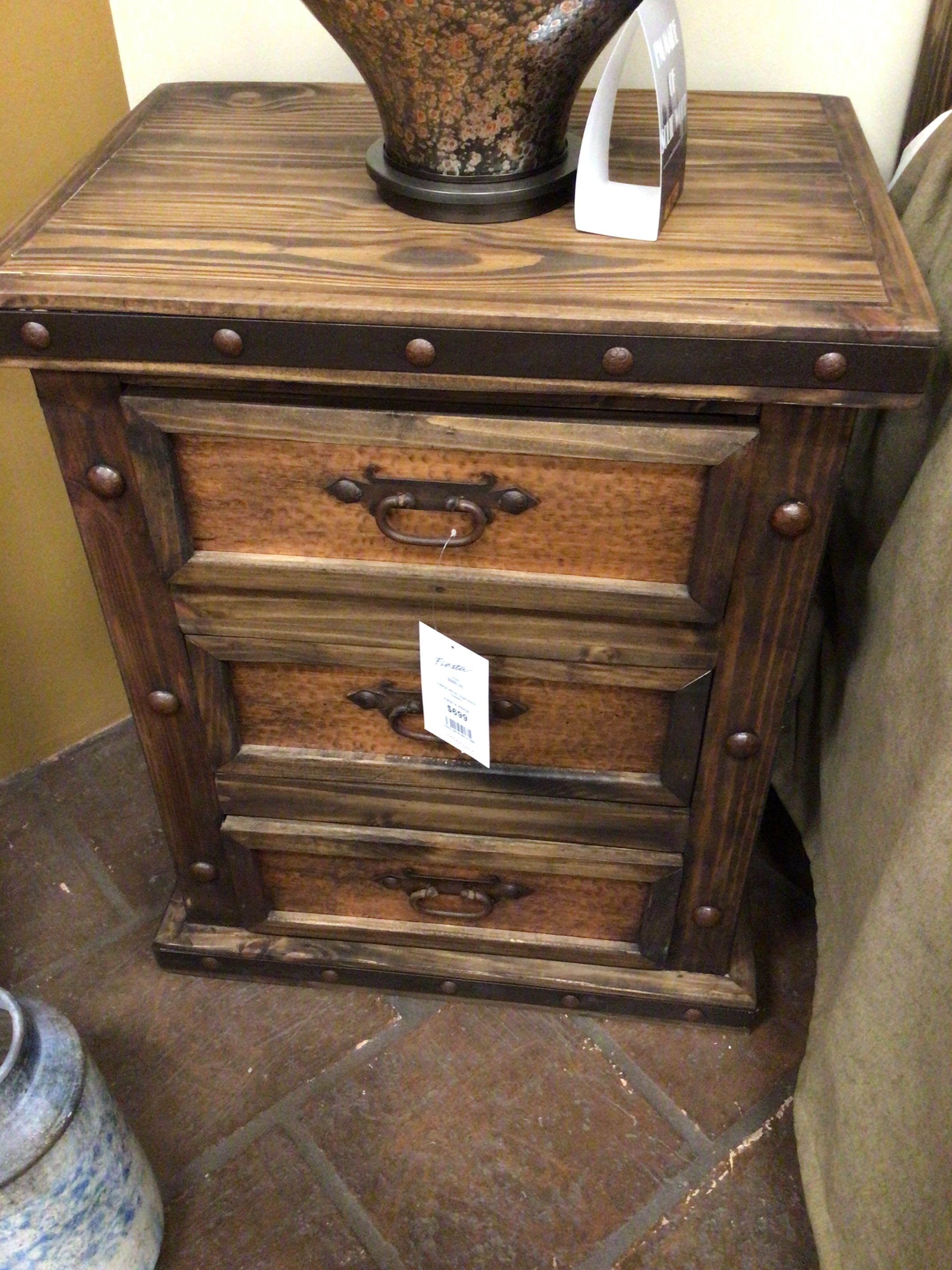 Wooden nightstand with three drawers on a tiled floor.
