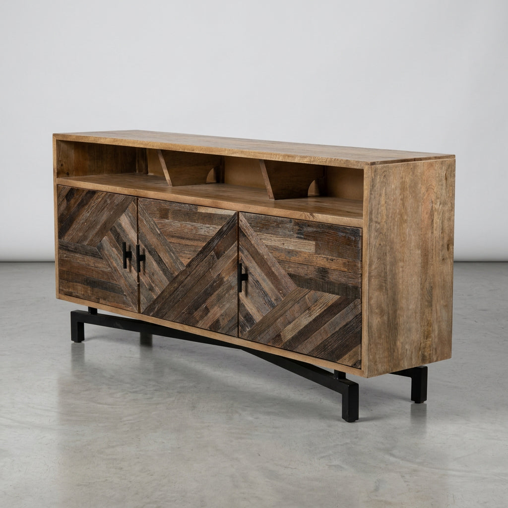 A rustic wooden chest of drawers with a geometric chevron pattern on the drawer fronts, shown in a warehouse or workshop setting with protective plastic wrapping on some furniture in the background.