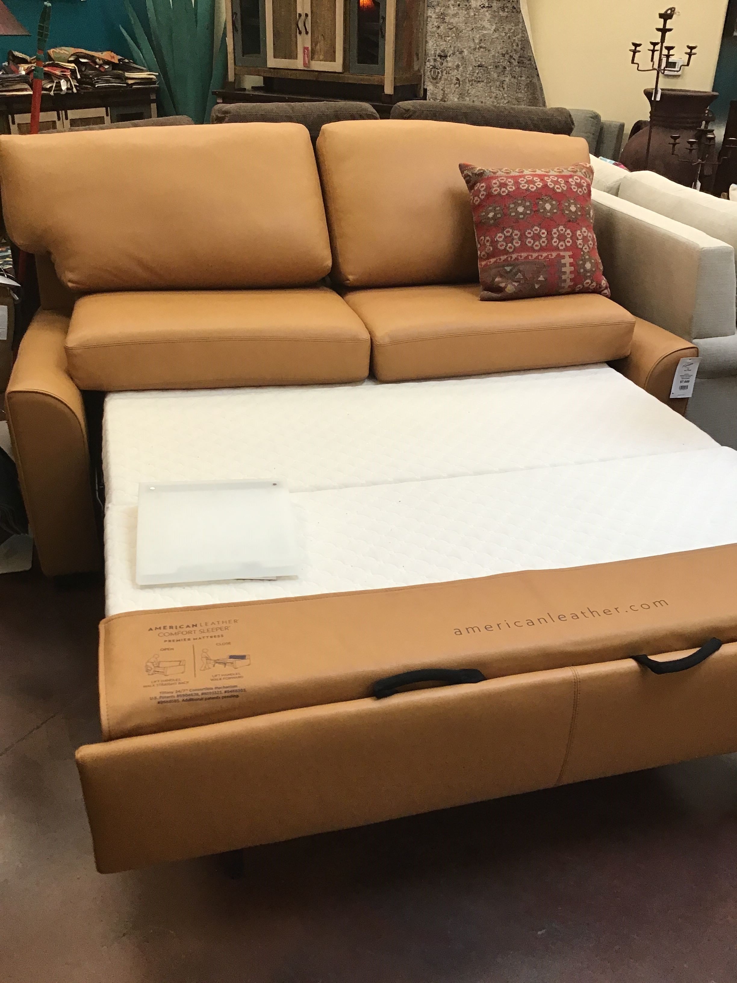 Brown leather sectional sofa with a pull-out bed mechanism in a showroom setting.