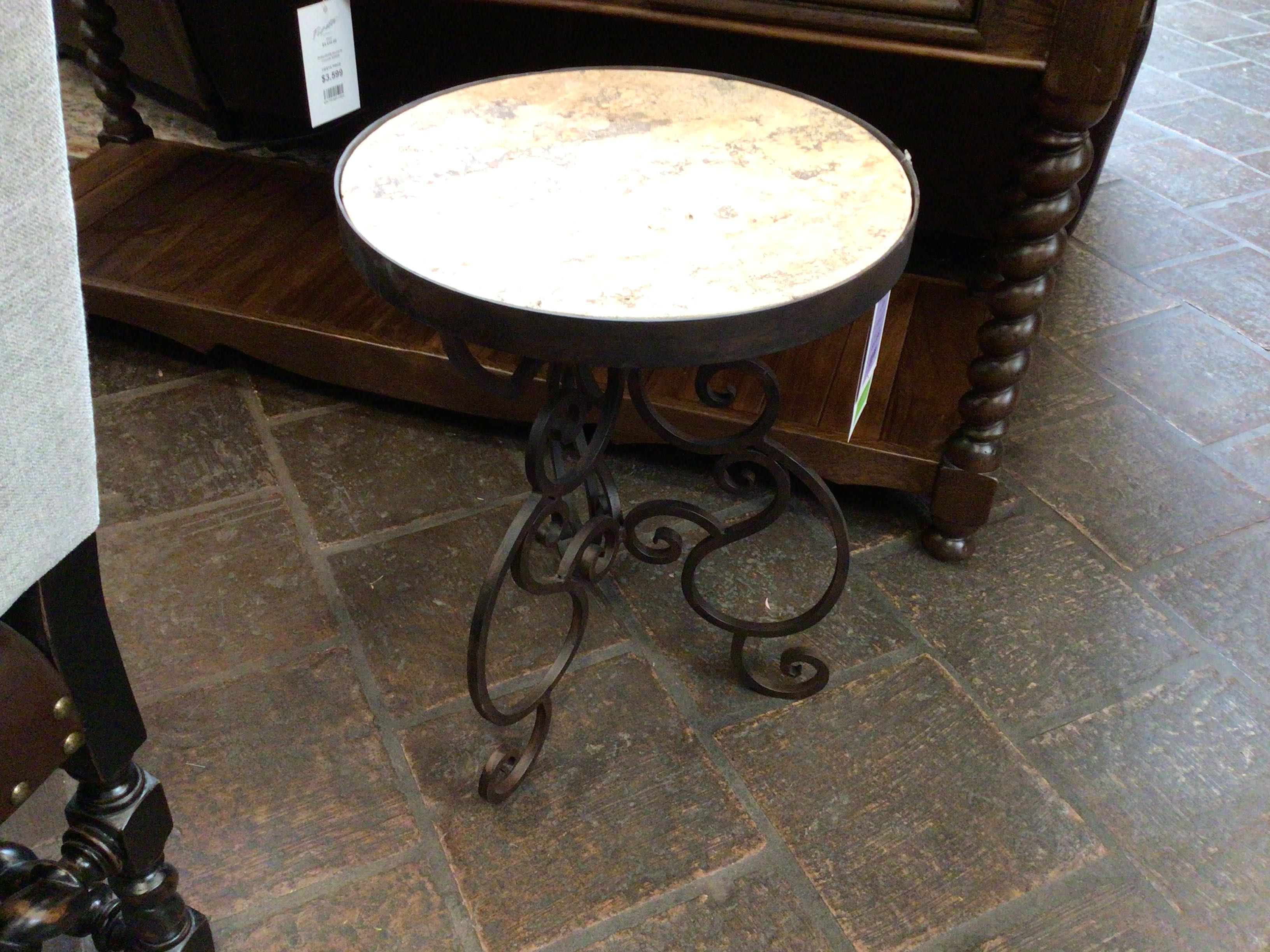 Small round table with travertine top and decorative metal legs on a stone floor.