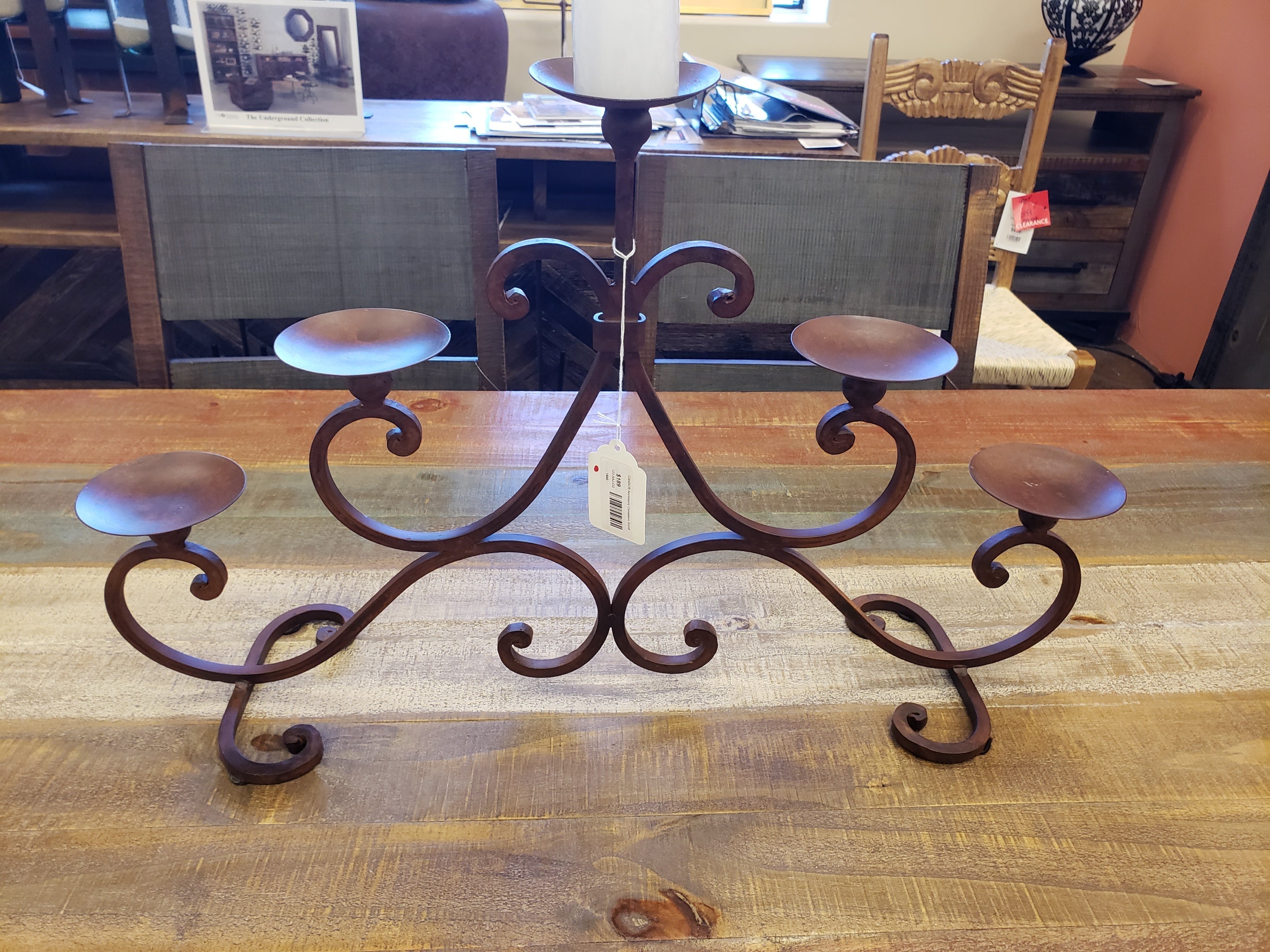 Decorative metal candelabra on a wooden table with a chair and other items in the background.