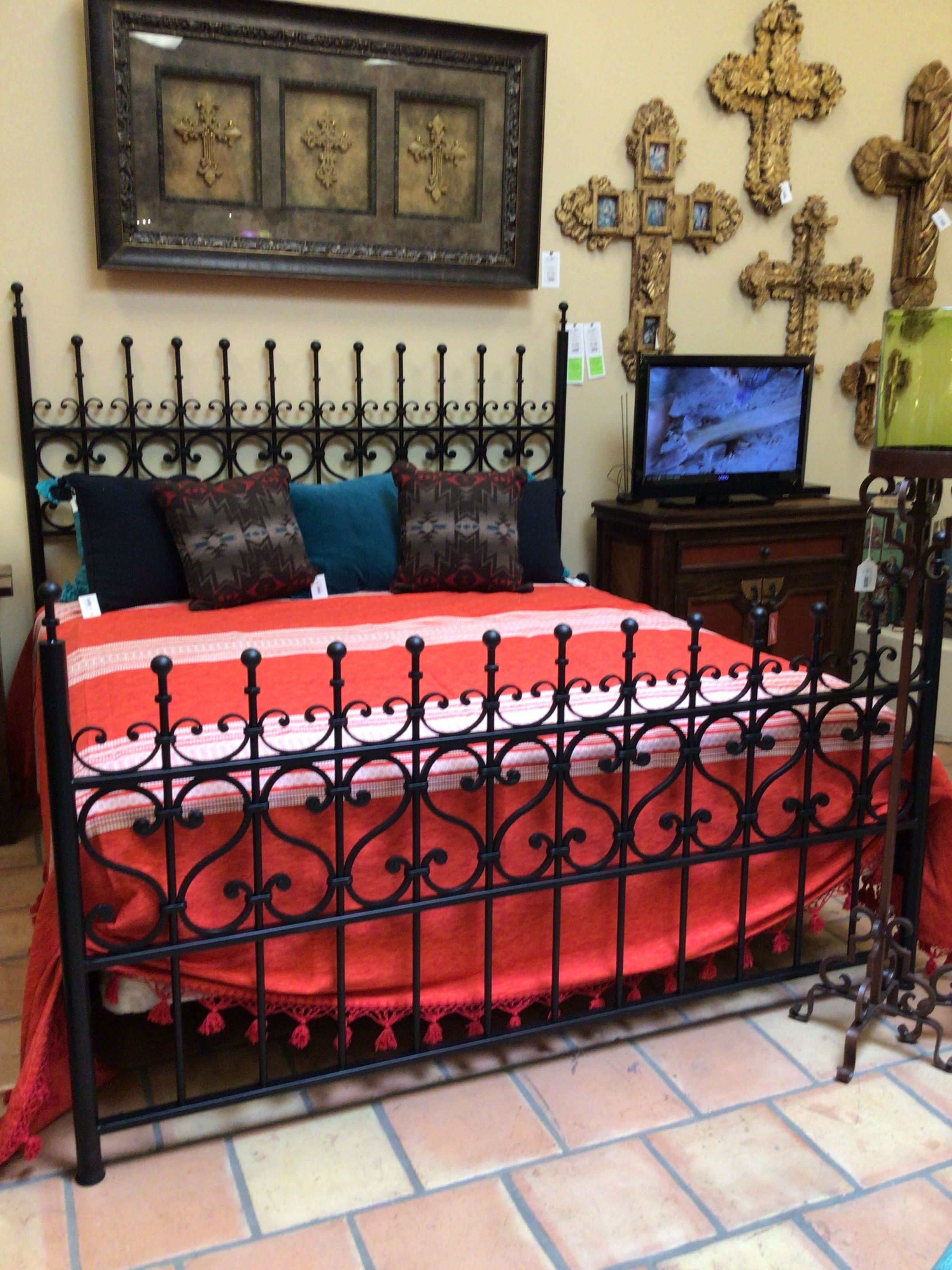 Wrought iron bed with decorative pillows and a red blanket in a store setting.