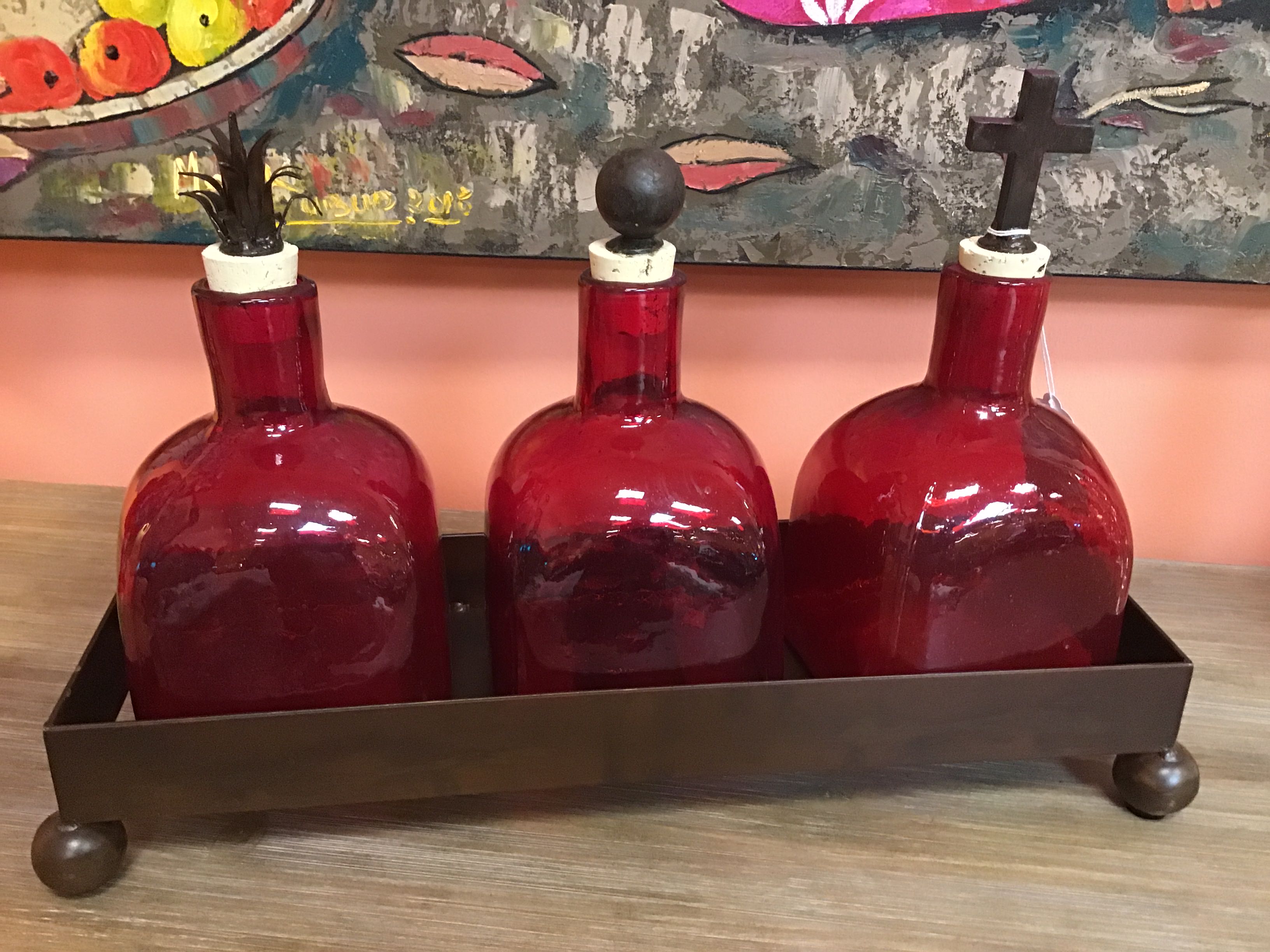 Three glass bottles with iron stoppers on a metal tray against a colorful abstract painting.