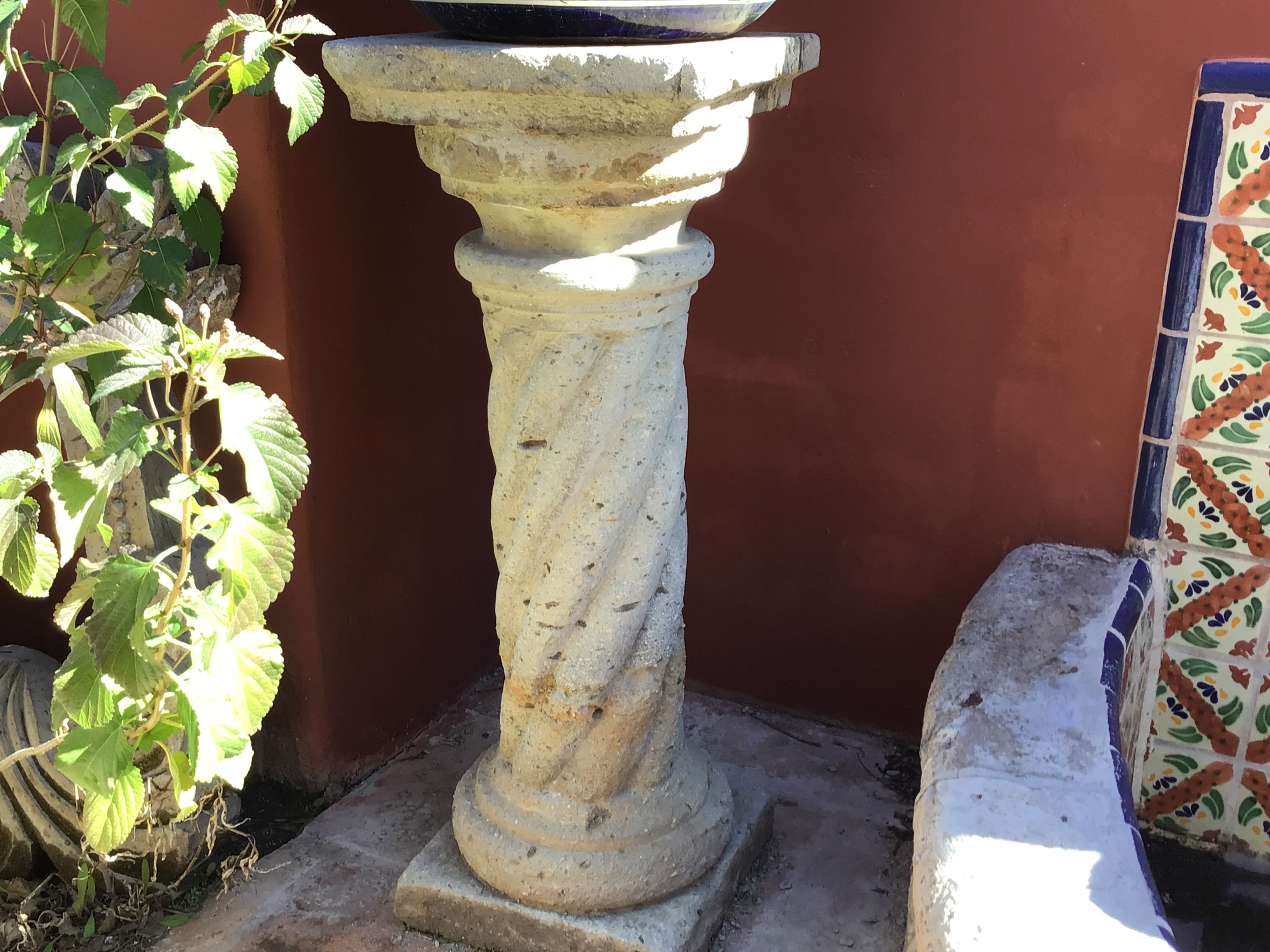 Decorative stone pedestal with a plant and tiled object in the background