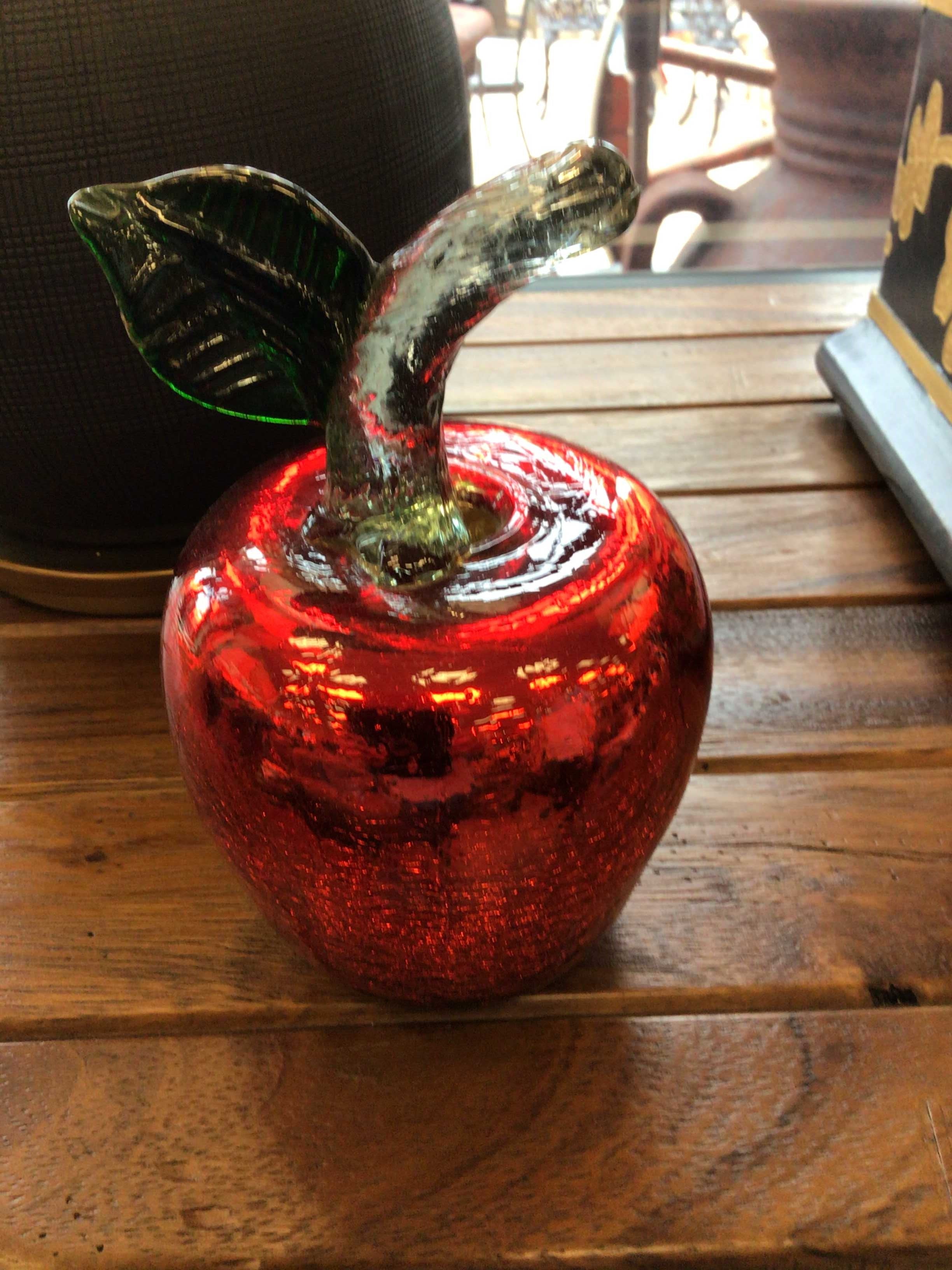 Red glass apple with a green leaf on a wooden surface