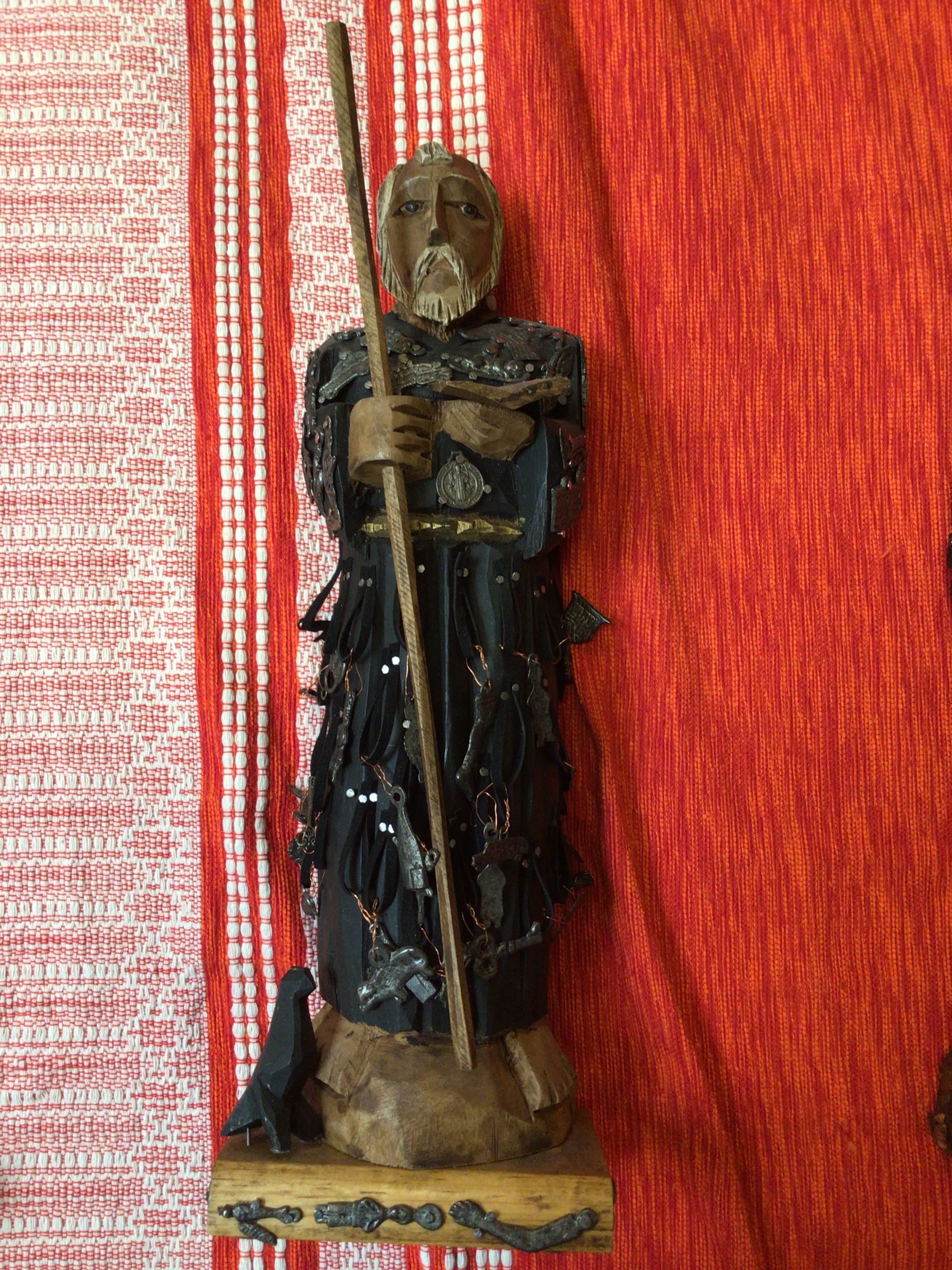 Wooden figurine of a warrior holding a spear against a red and white striped background