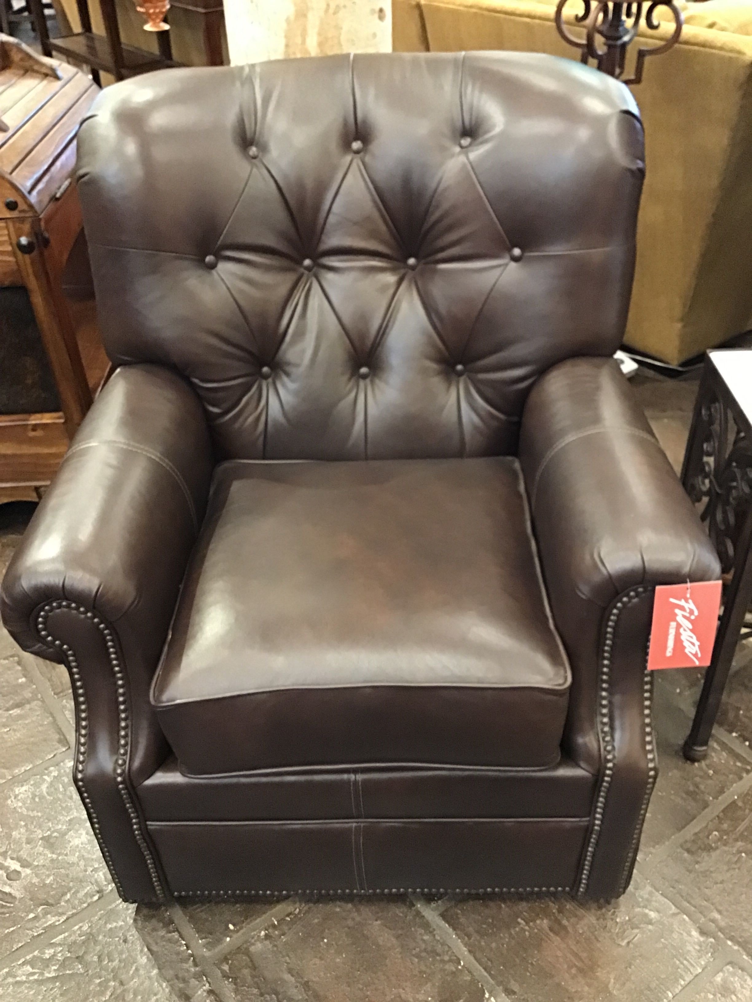 Brown leather armchair with a visible tag on a stone floor.