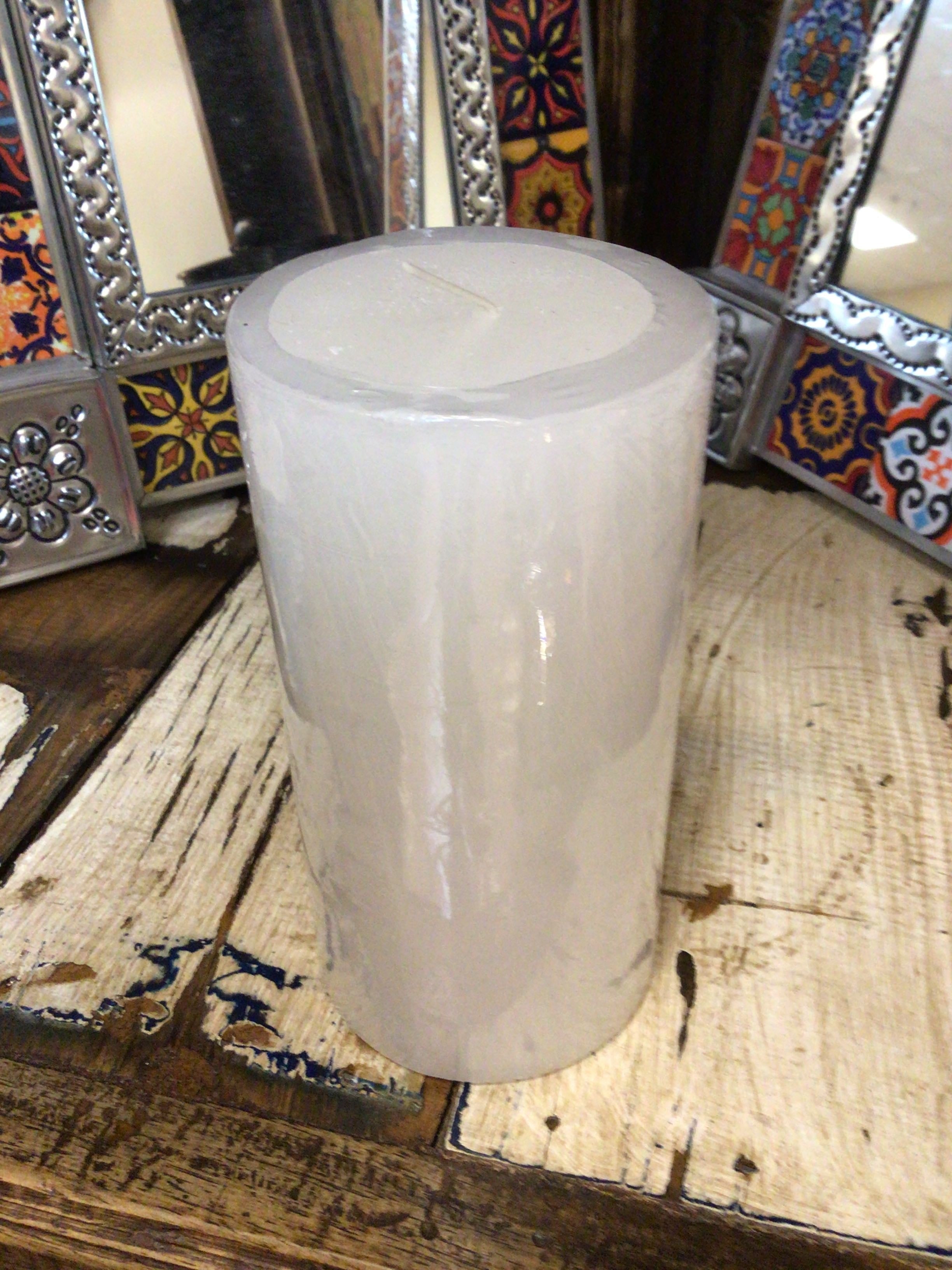 White candle on a wooden surface with decorative mirrors in the background