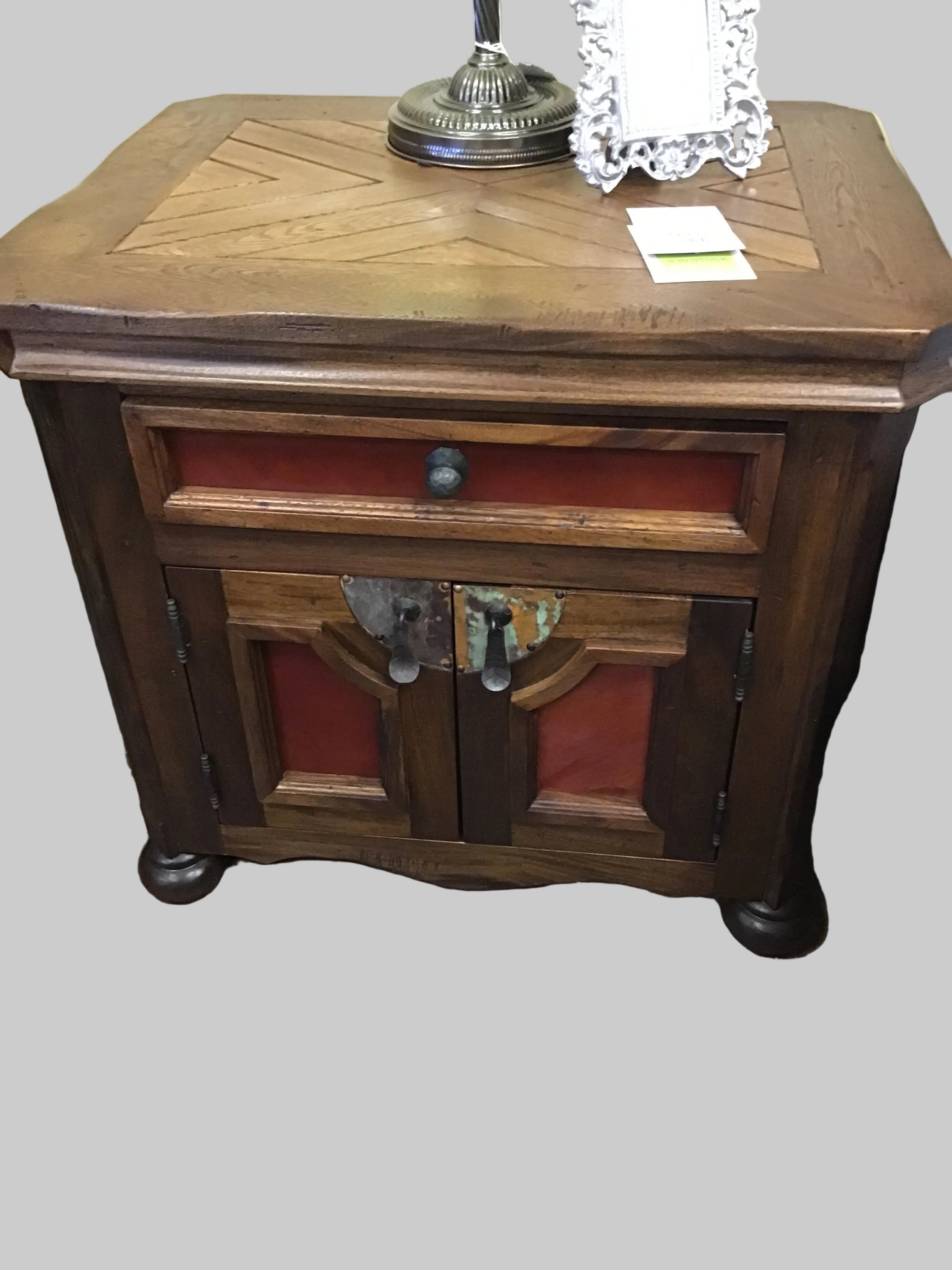 Wooden side table with a drawer and two doors on a stone floor.