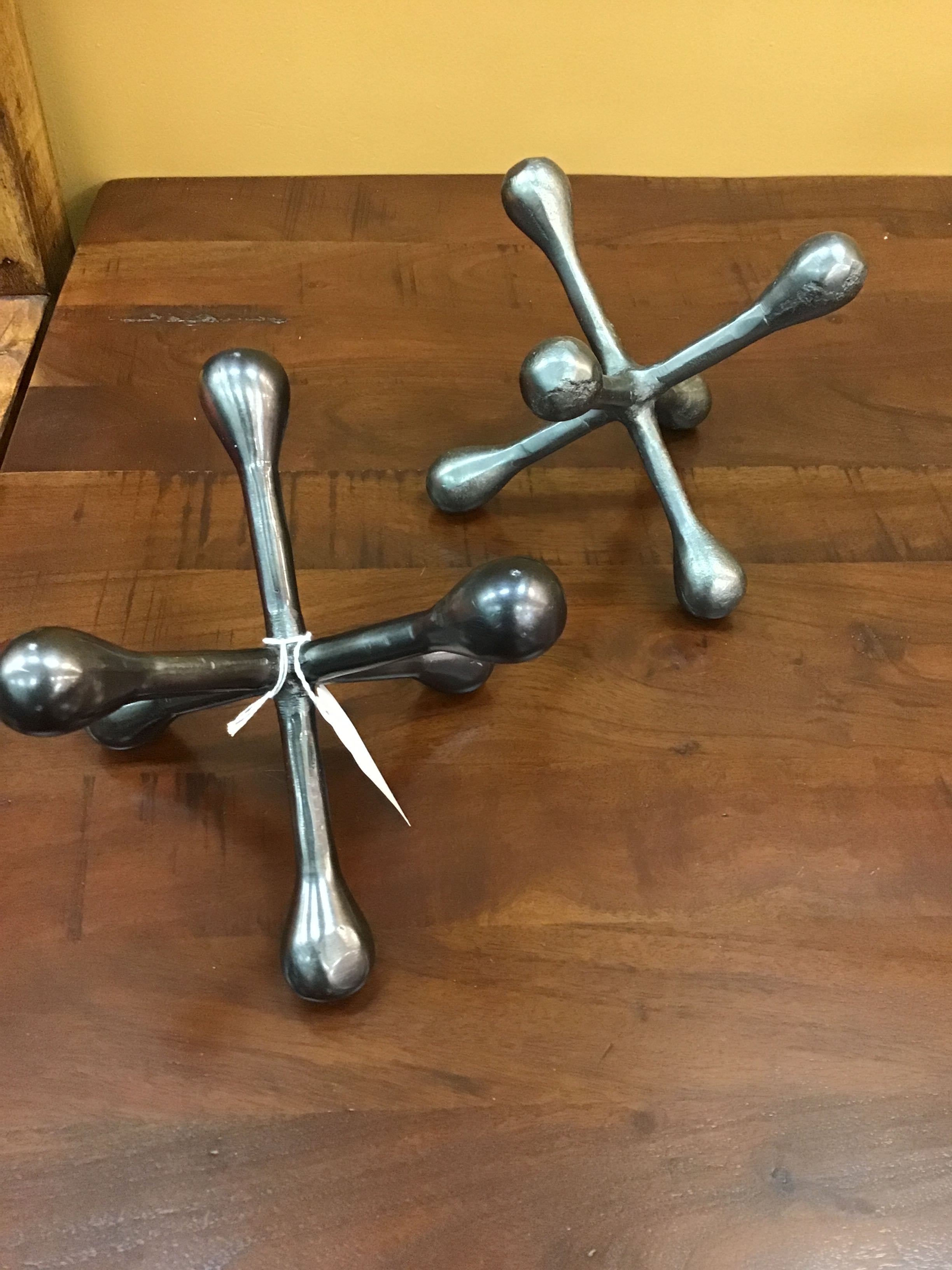 Two metallic cross-shaped wall hooks on a wooden surface.