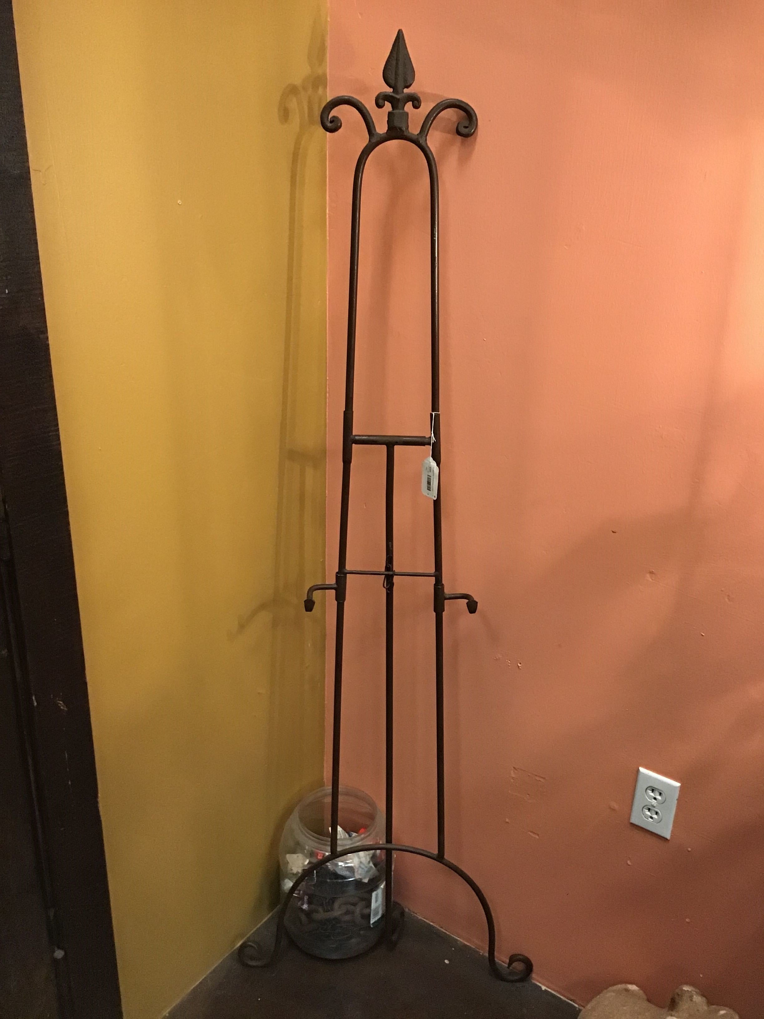 Wrought iron coat rack against a wall with a light switch.