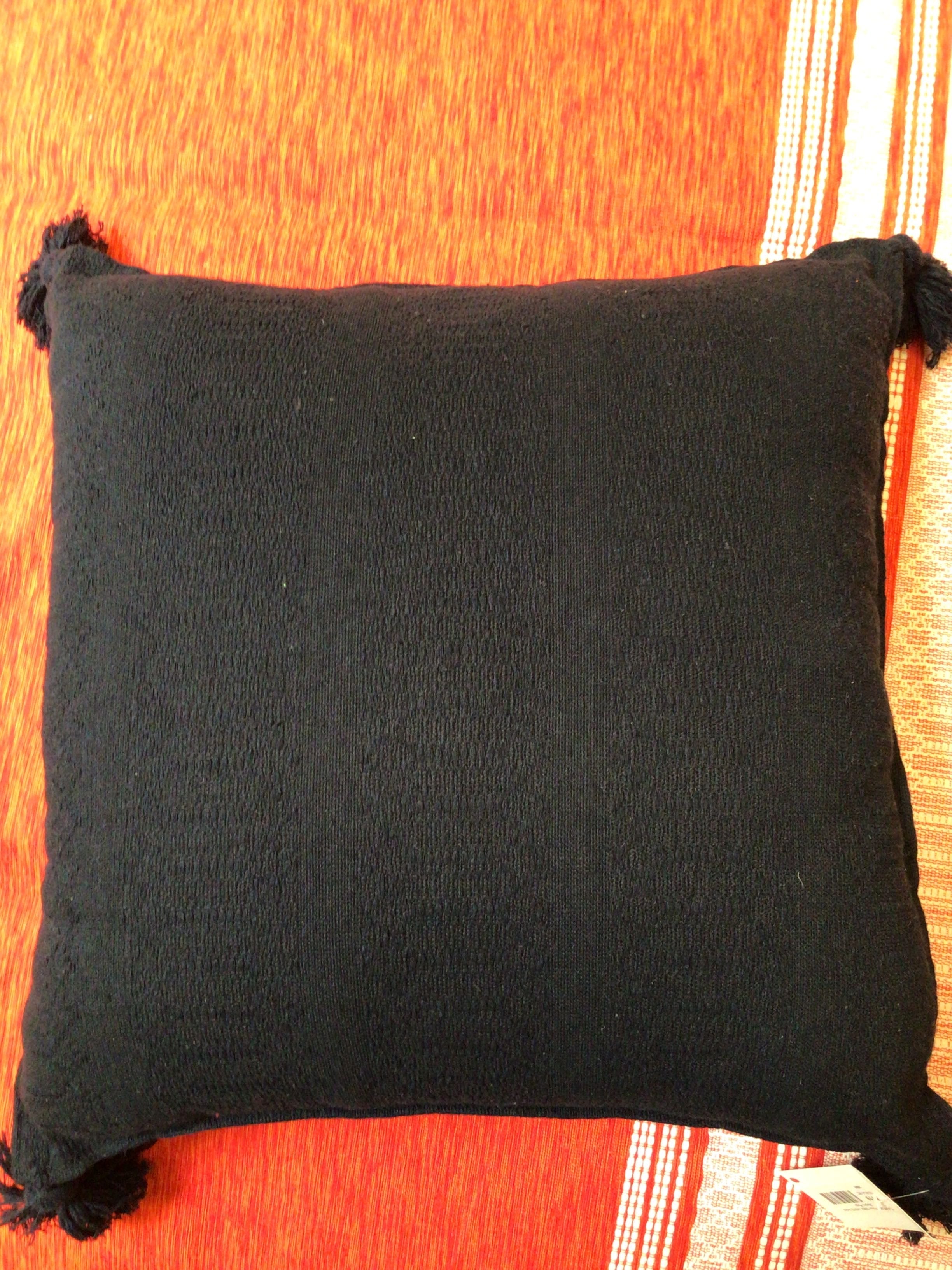 Black pillow with tassels on a red fabric background