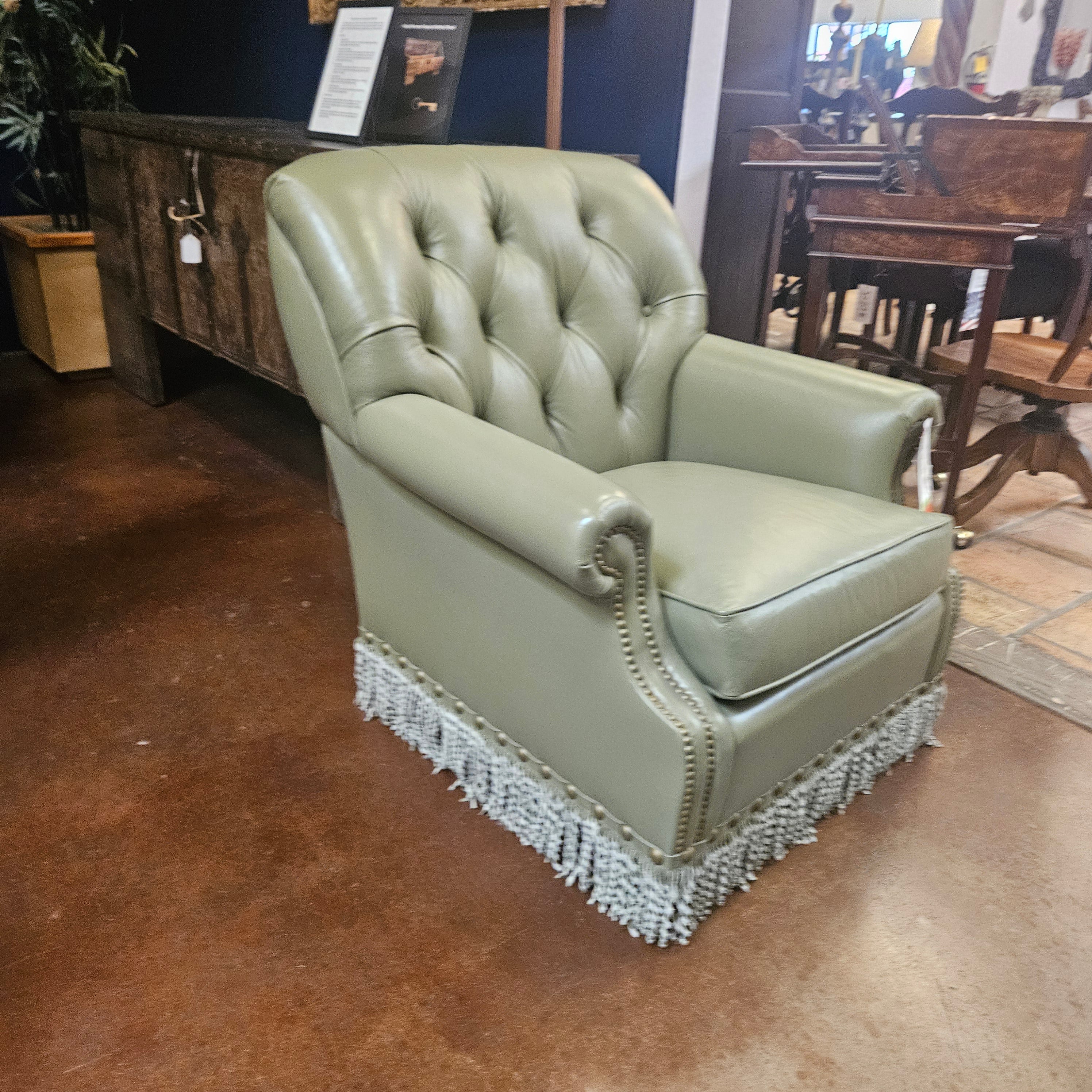 Green leather armchair with fringe trim in a store setting