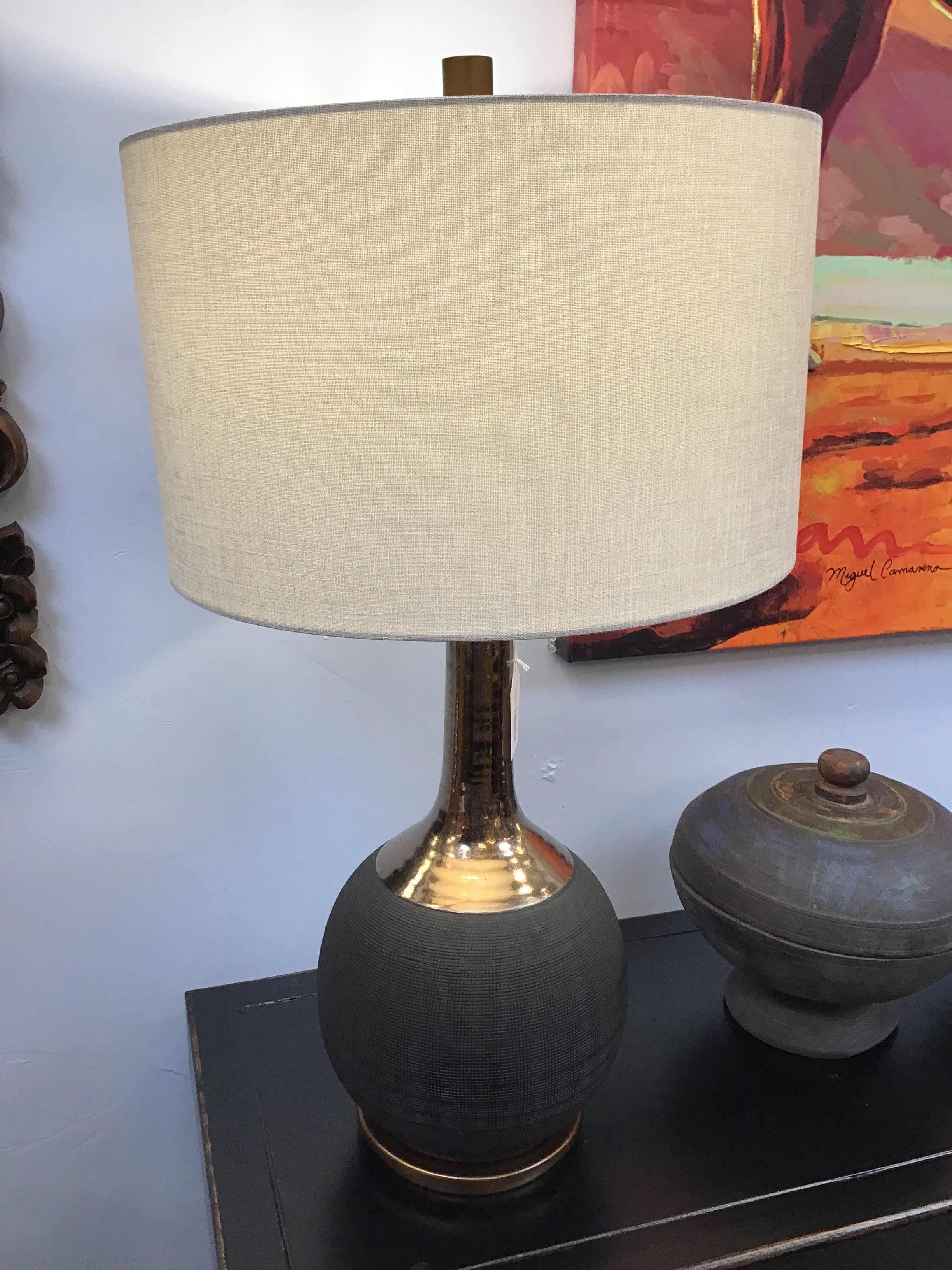 Table lamp with beige shade on a dark surface against a light blue wall.