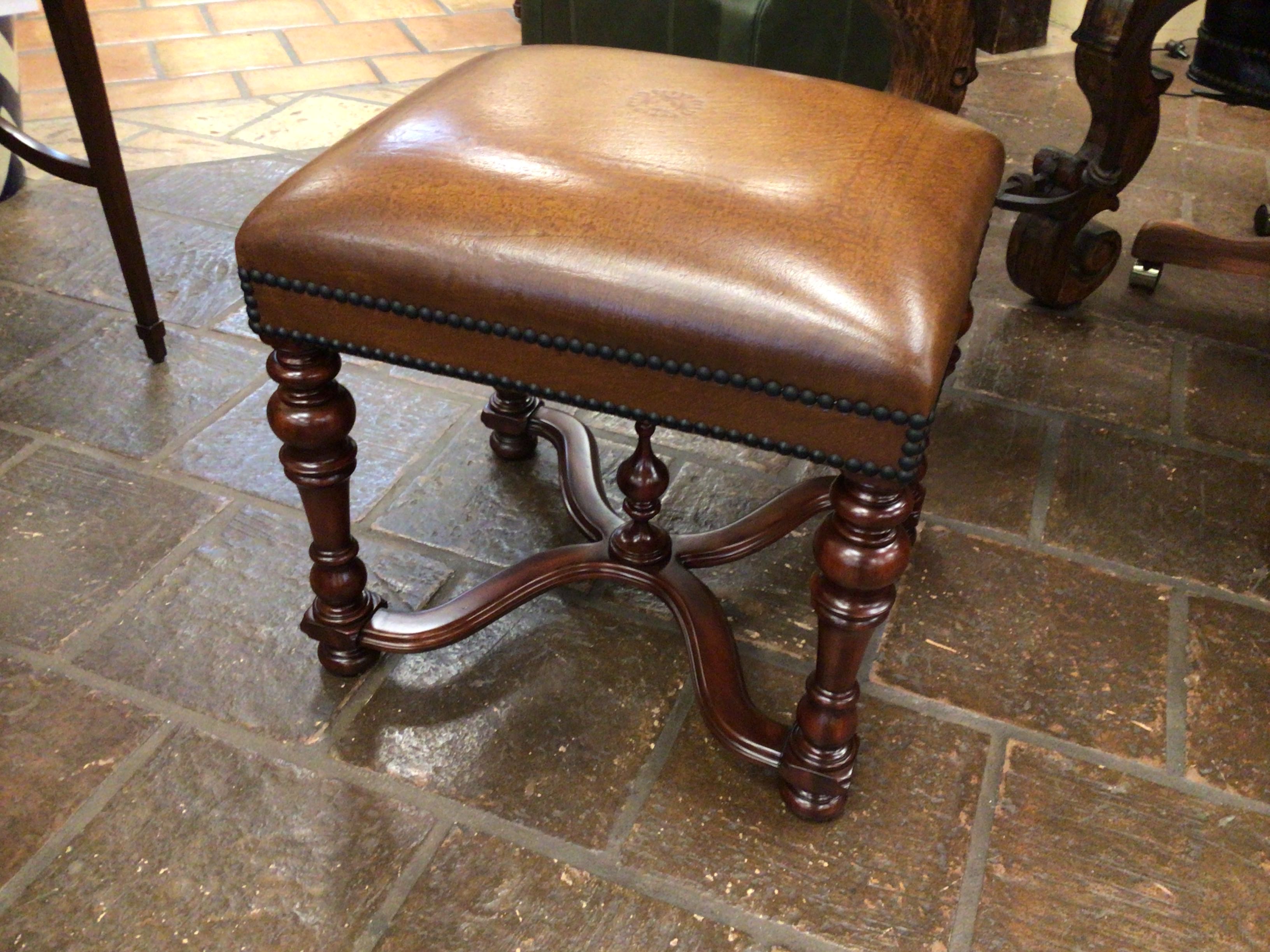 Brown leather stool with etched leather and wooden legs on a stone floor. 