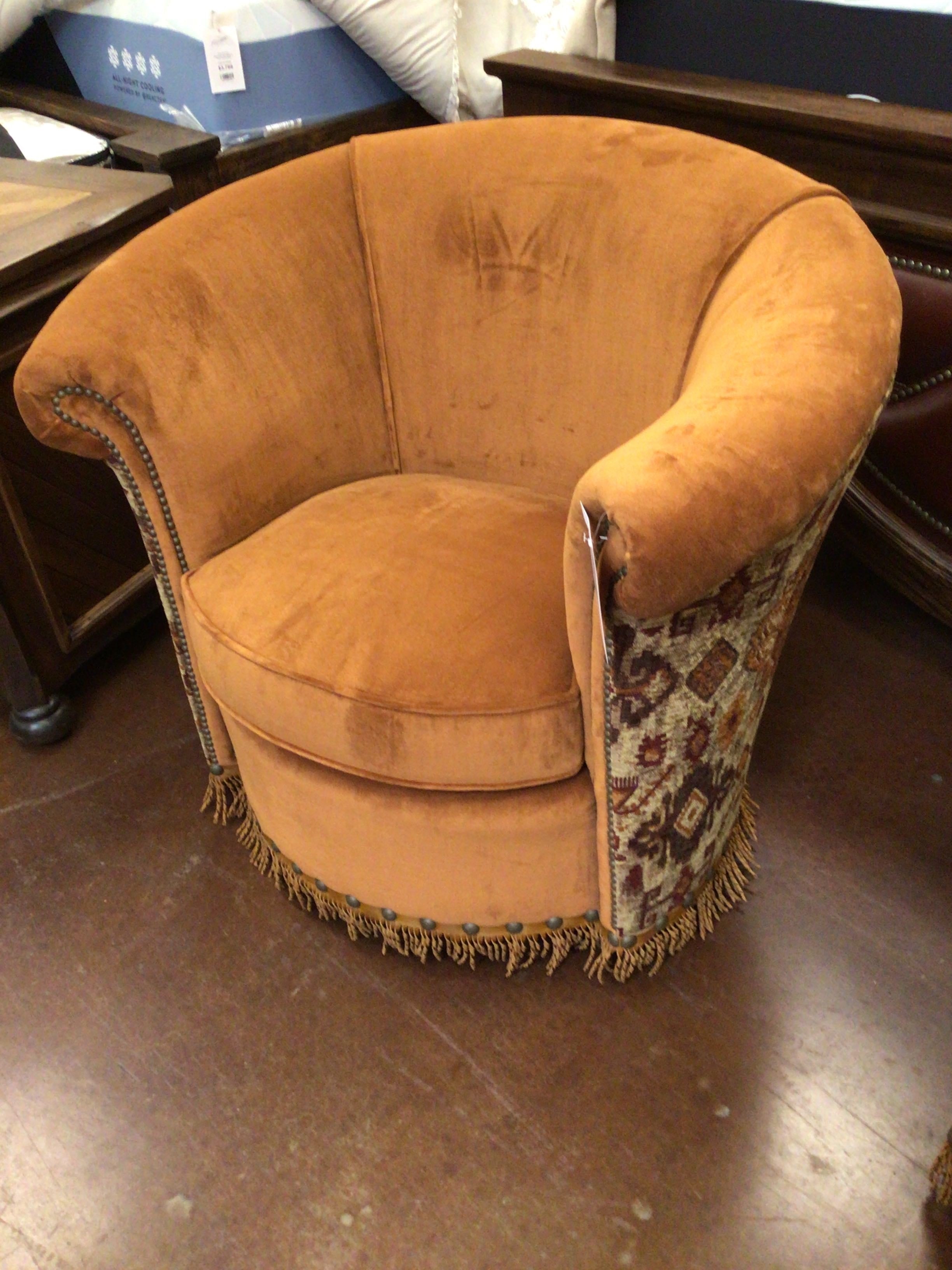 Brown velvet armchair with patterned fringe on a wooden floor