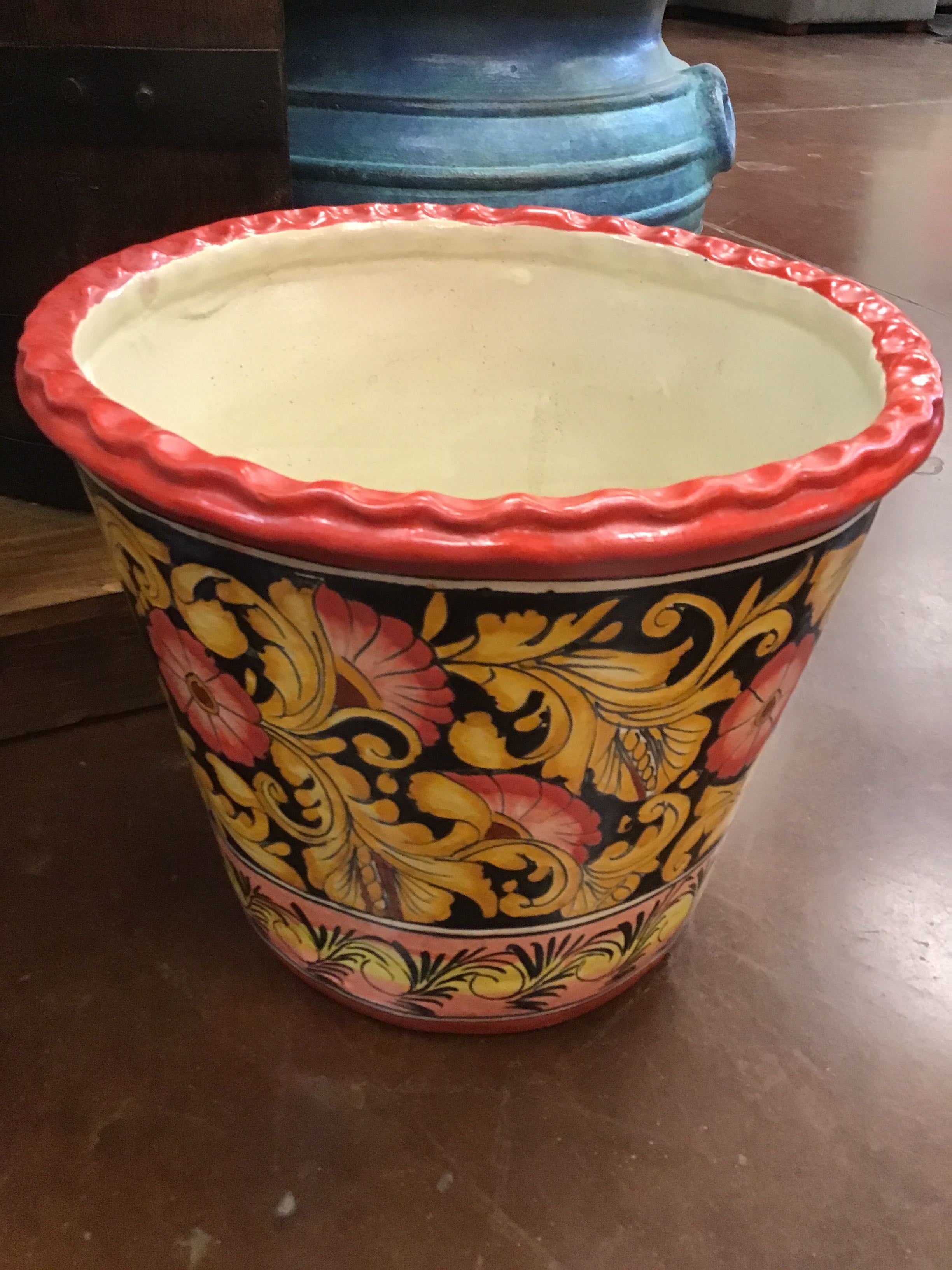Decorative pot with red rim and colorful floral design on a wooden surface