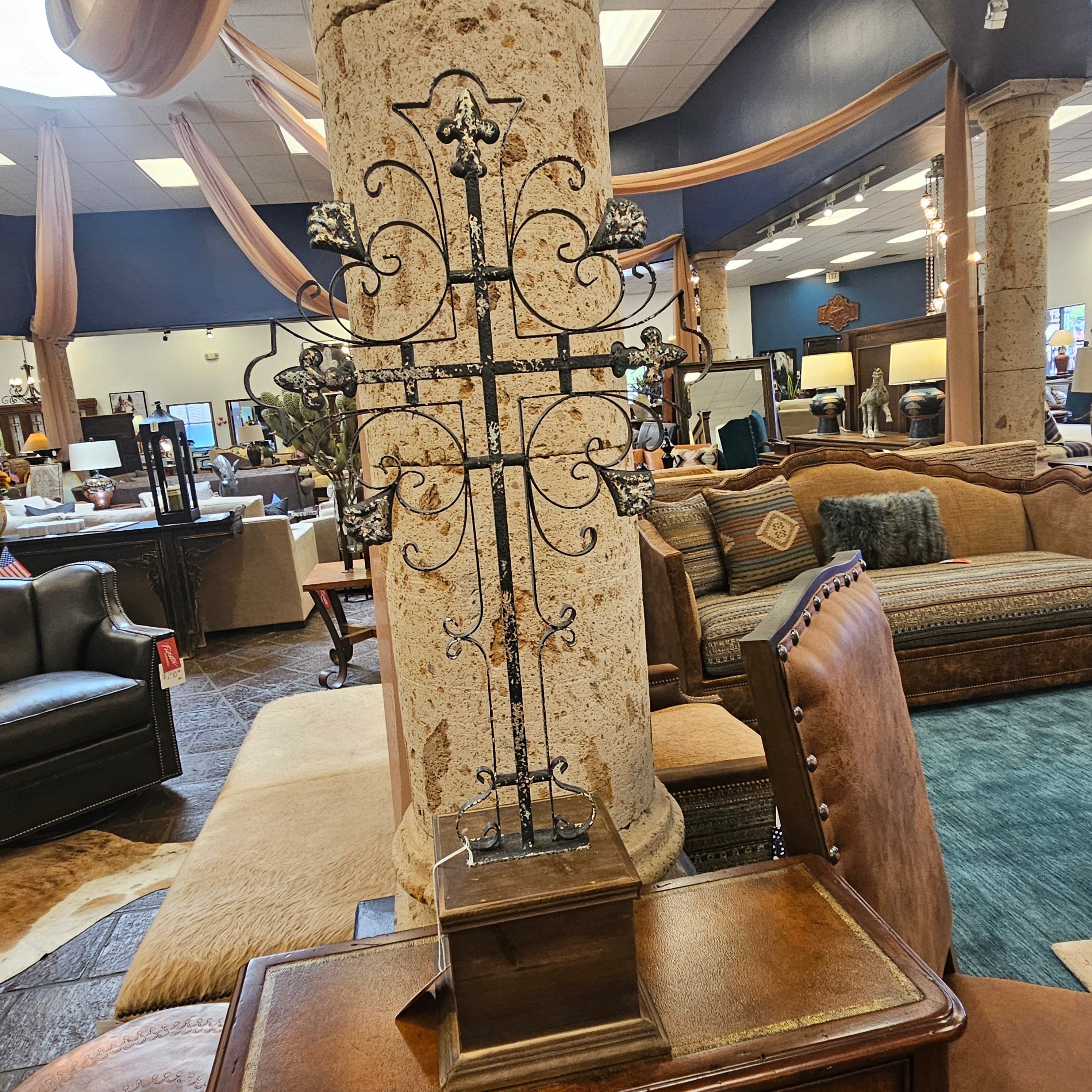 Decorative cross with intricate metalwork on a stone pedestal in an indoor setting.