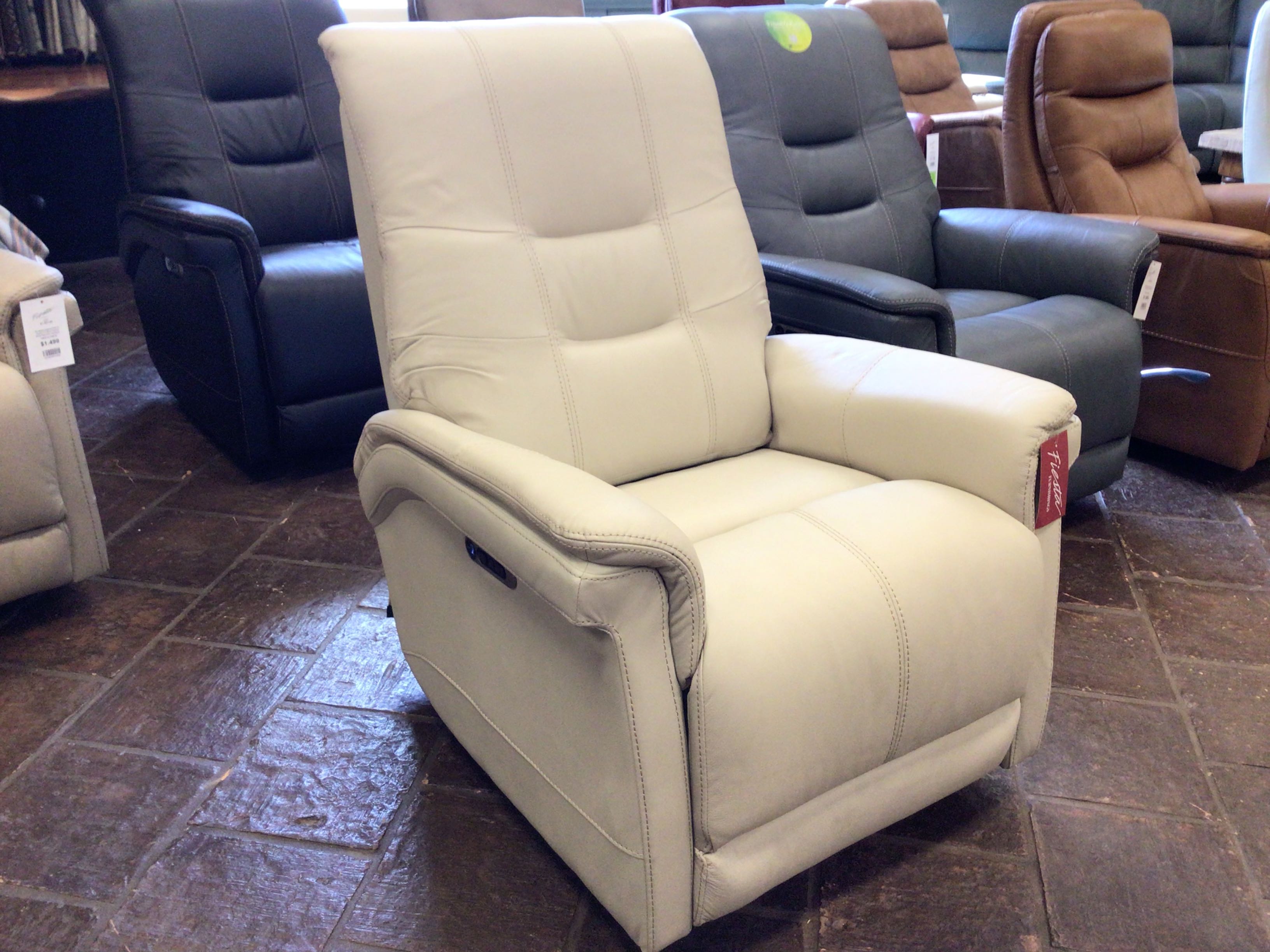 Beige recliner chair in a showroom setting with other chairs.