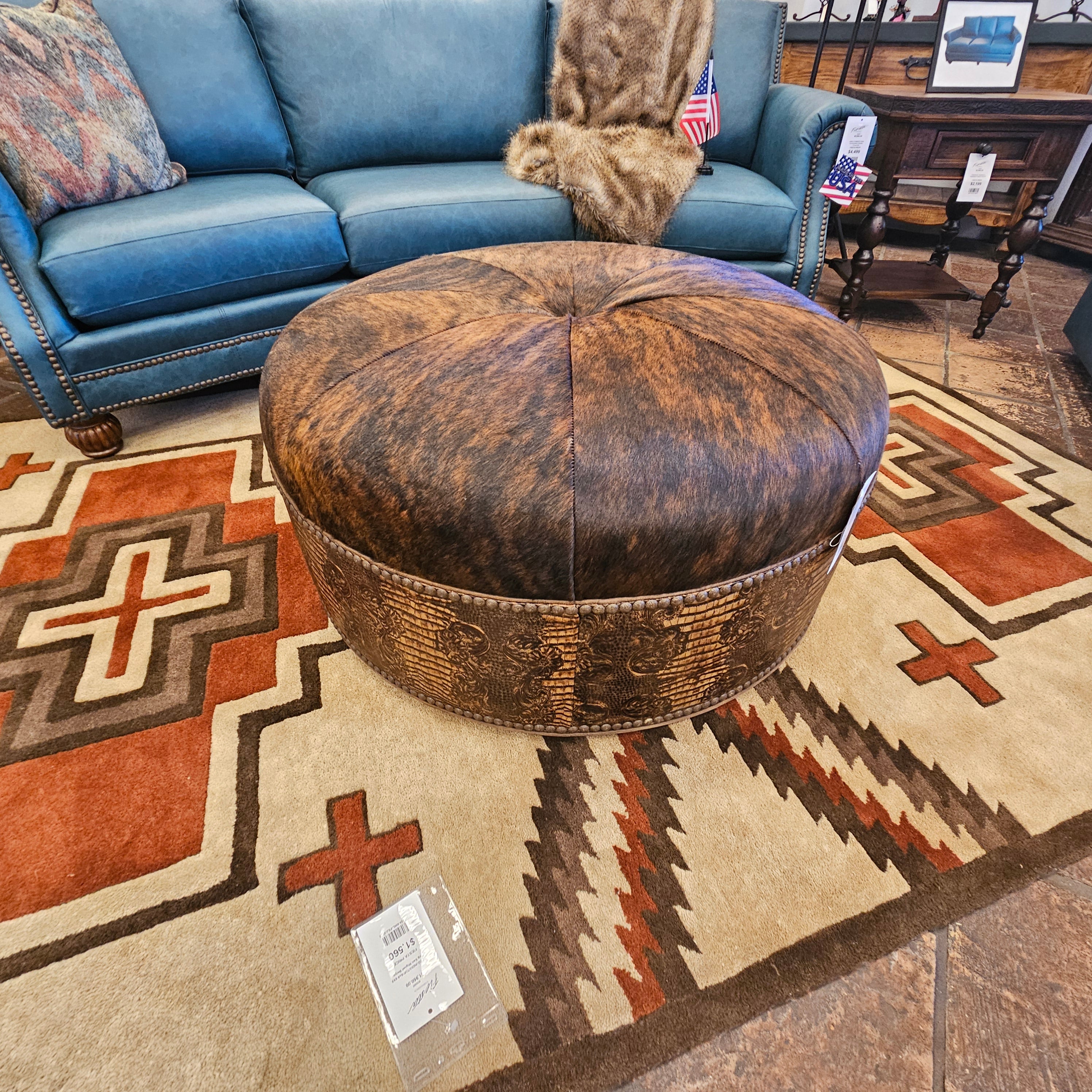 Round wooden ottoman on a patterned rug with a blue sofa in the background.