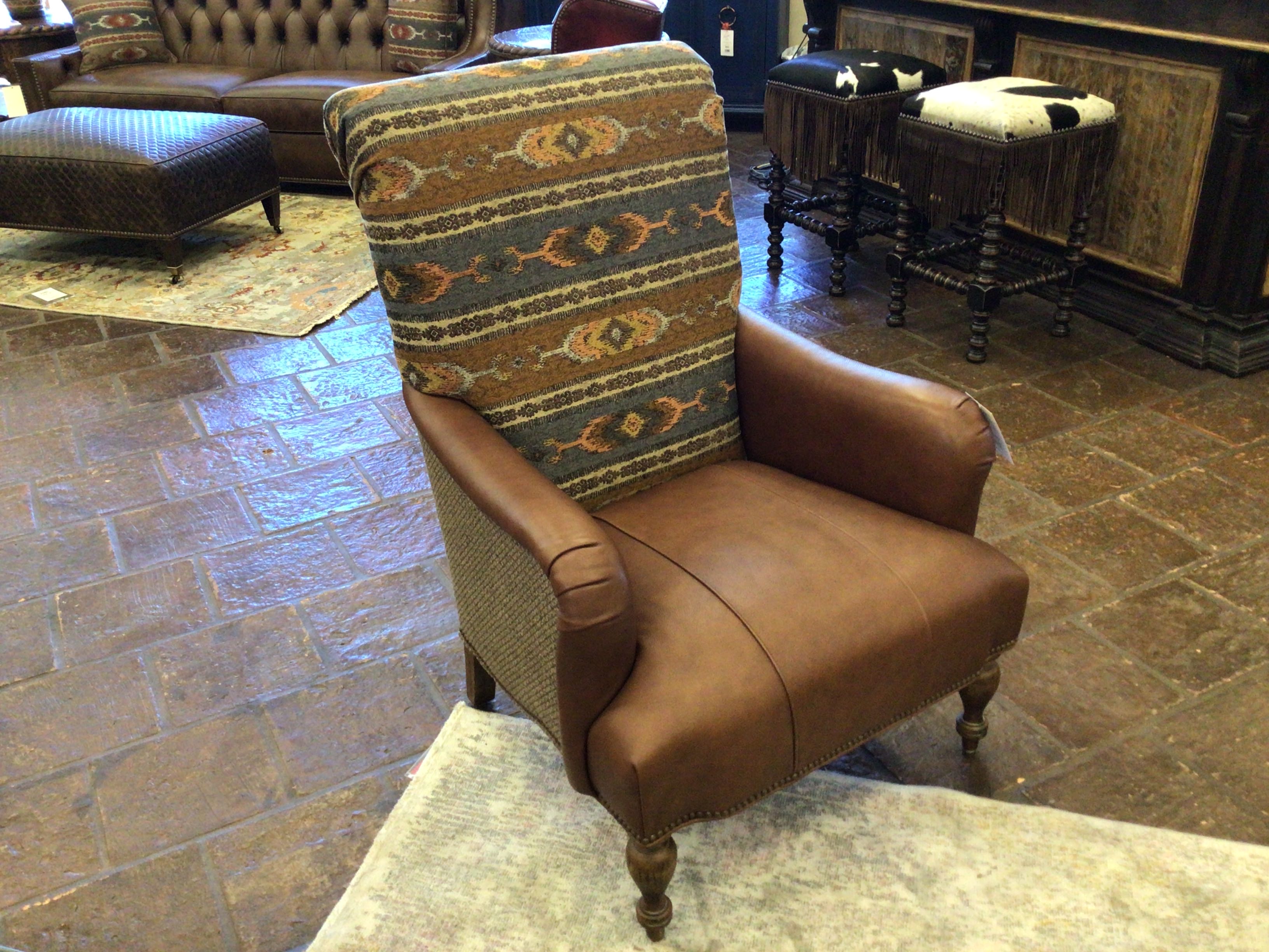 Brown leather armchair with patterned backrest in a room with stone flooring and furniture.