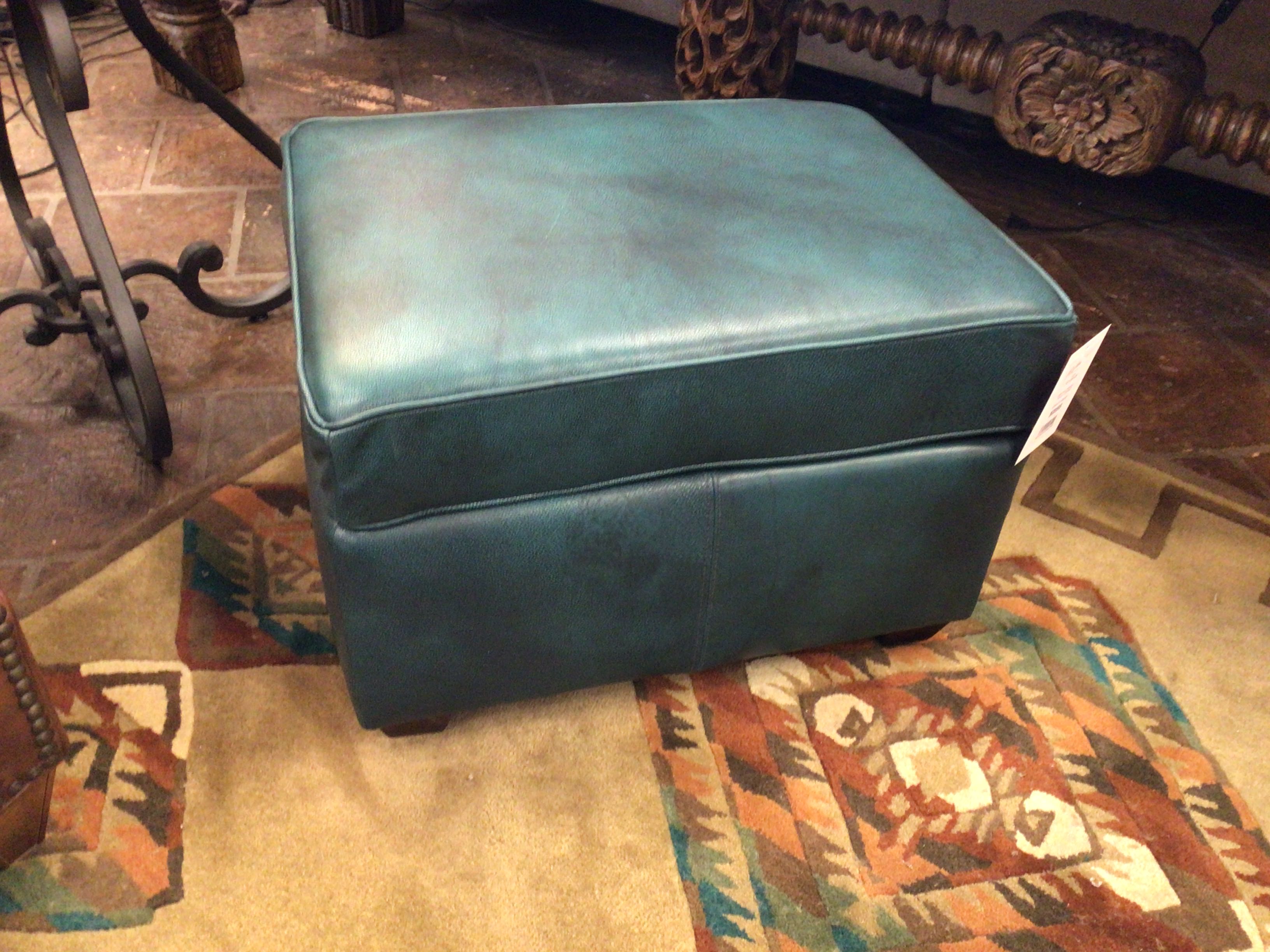Teal ottoman on a patterned rug with a decorative chair in the background